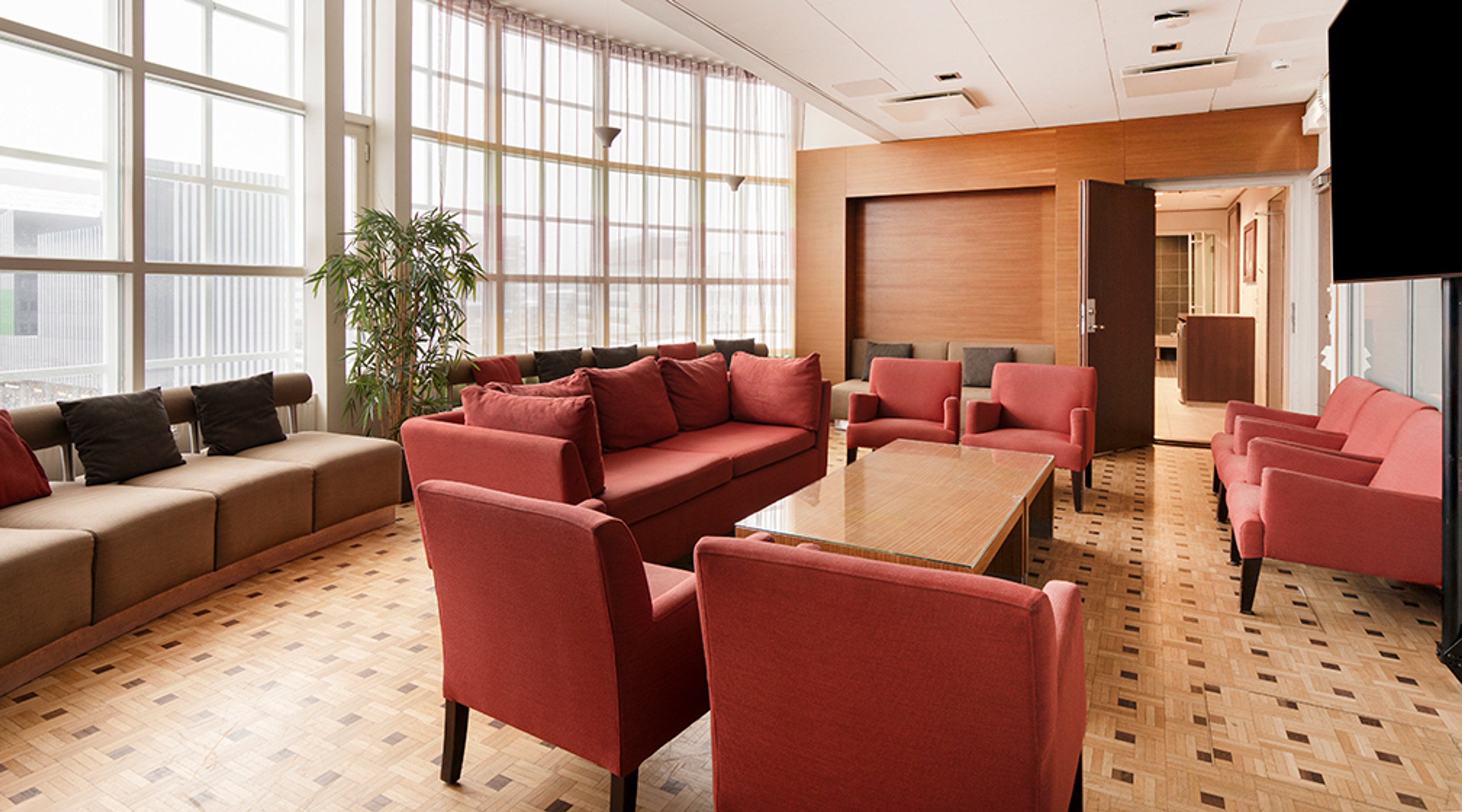 Valoisa odotustila, jossa punaiset ja ruskeat sohvat, puupöytä, parkettilattia ja isot ikkunat. Leveät kulkuväylät, ei kynnyksiä.