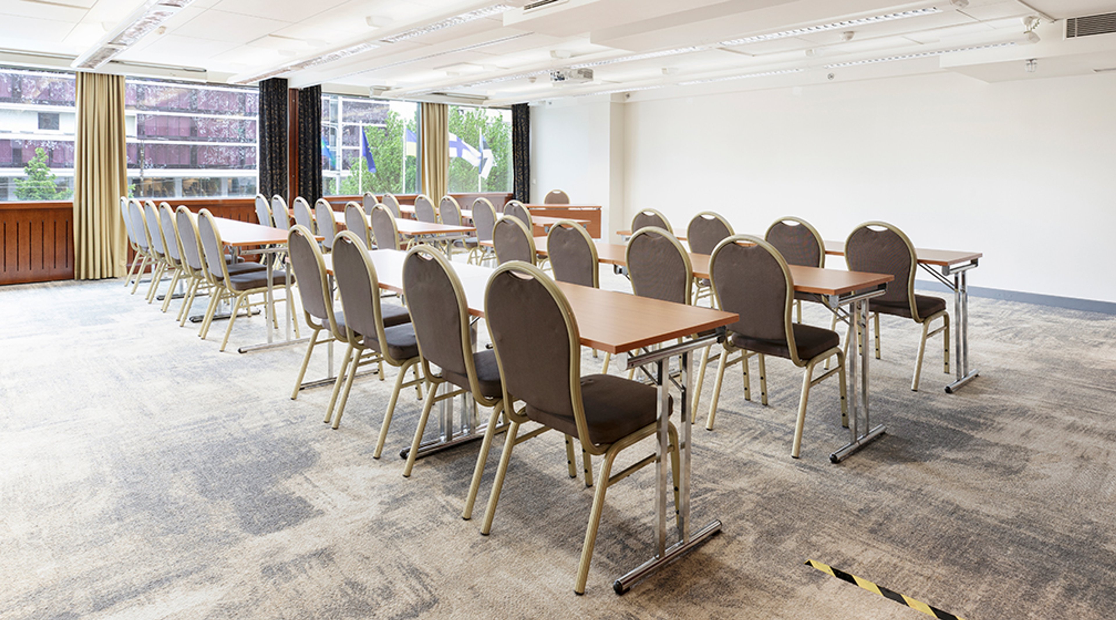 Conference room with long tables and upholstered chairs. Room has level carpeted flooring and large windows.