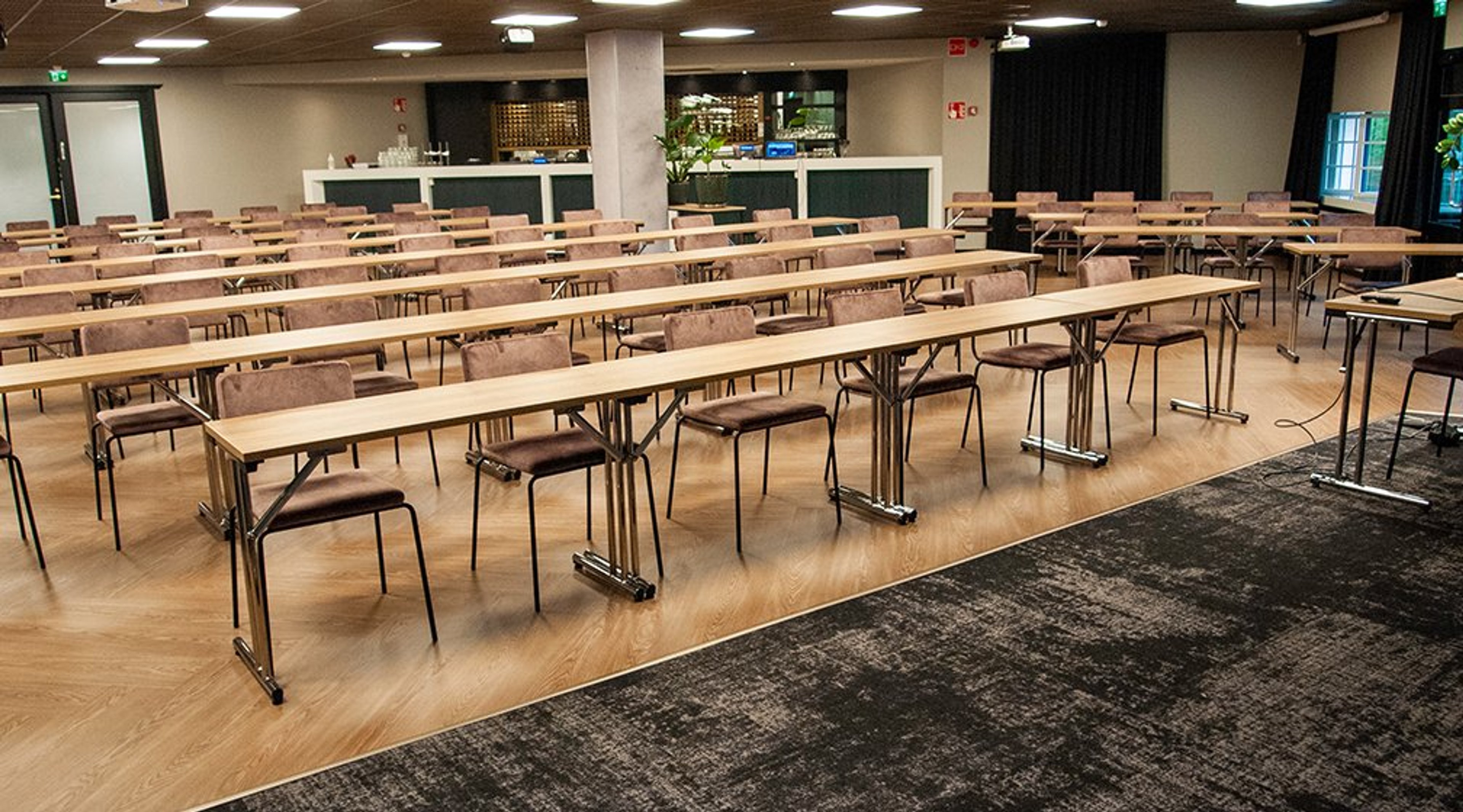 Kokoustila, jossa on riveittäin järjestettyjä pöytiä ja tuoleja, puulattia ja tumma matto. Taustalla näkyy tarjoilutiski.