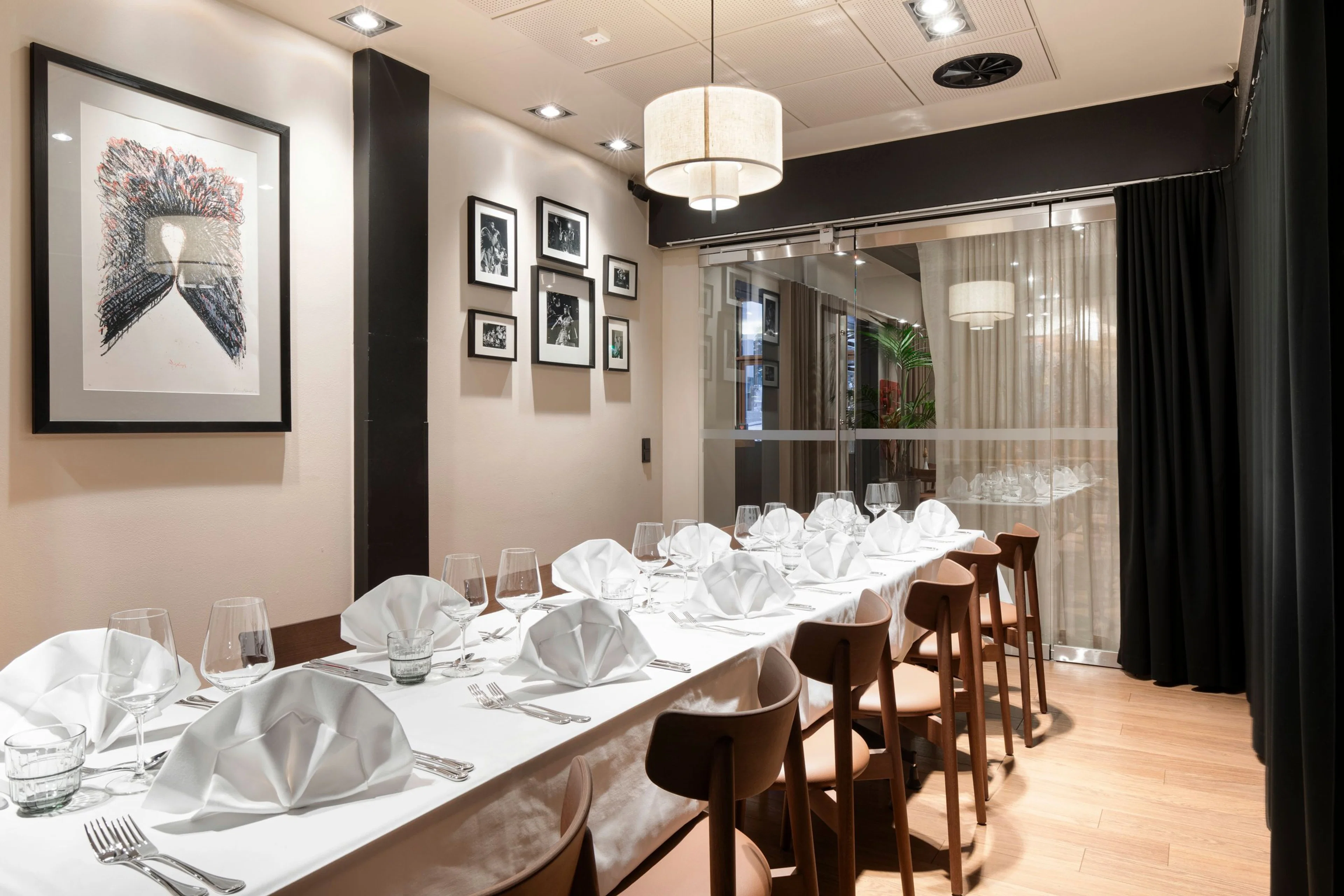 Tyylikkäästi katettu pitkä pöytä yksityisessä ravintolan kabinetissa. Vaaleat seinät, puulattia ja sisustuksessa taidetta.