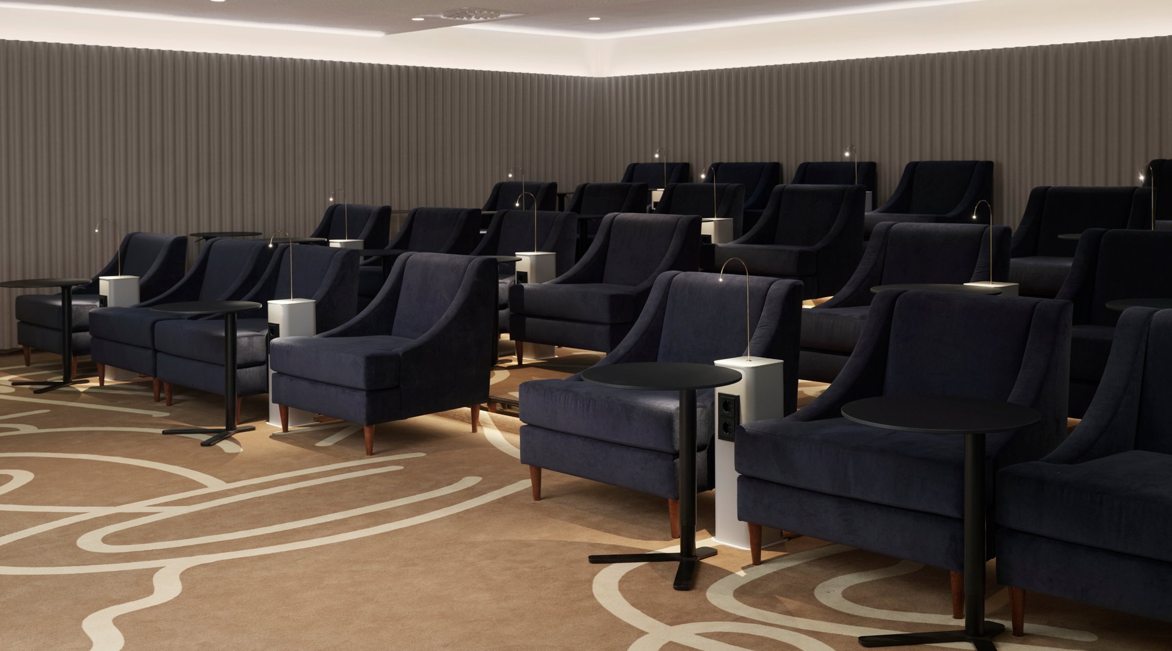 Moderni auditoriotila tummansinisillä nojatuoleilla, joiden välissä pieniä pöytiä ja lukuvalot. Lattialla kuvioitu matto.