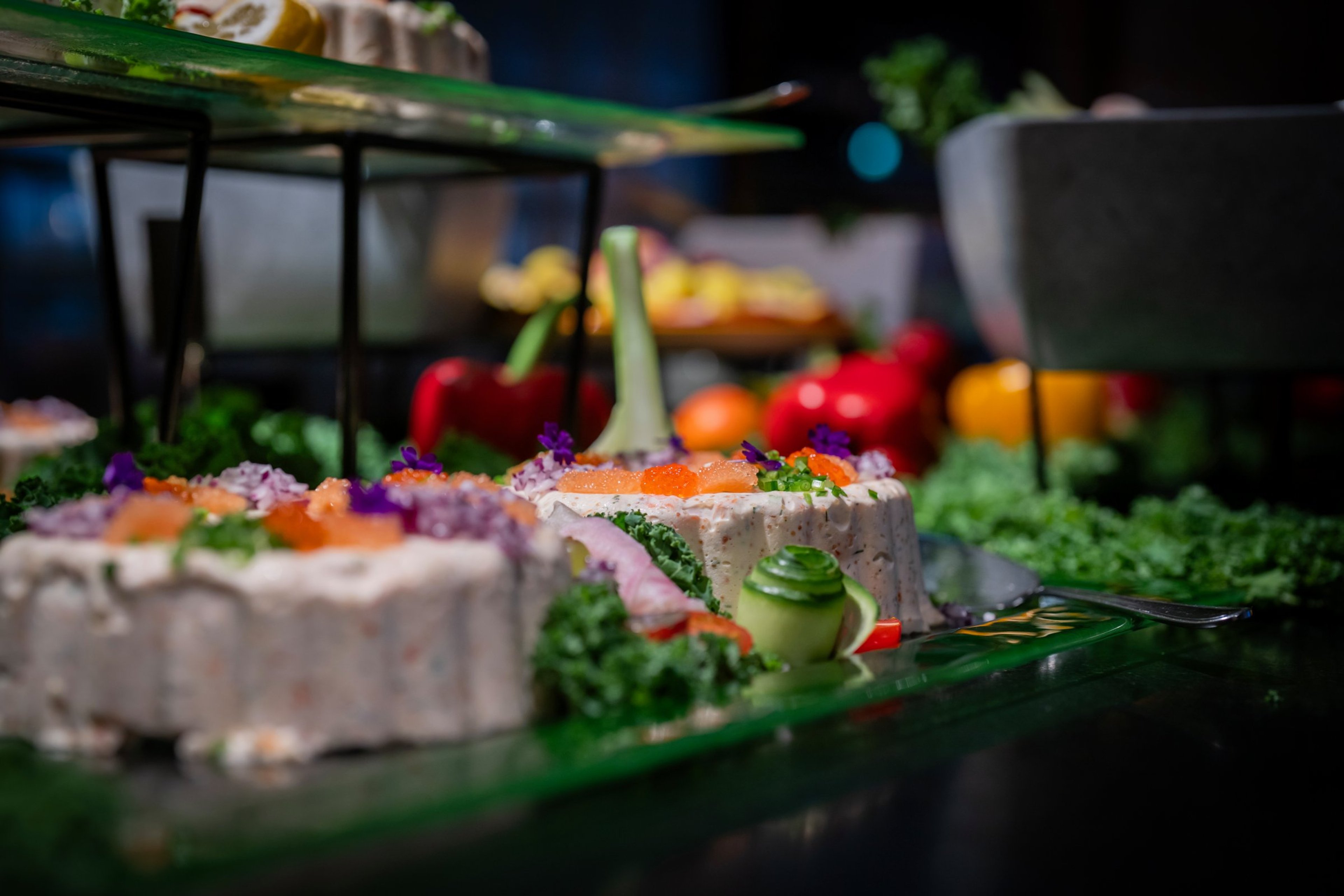 Kauniisti koristeltuja voileipäkakkupaloja tarjoilupöydällä. Etualalla näkyy suolaisia kakkuja koristeltuna yrteillä, kukilla ja vihanneksilla.