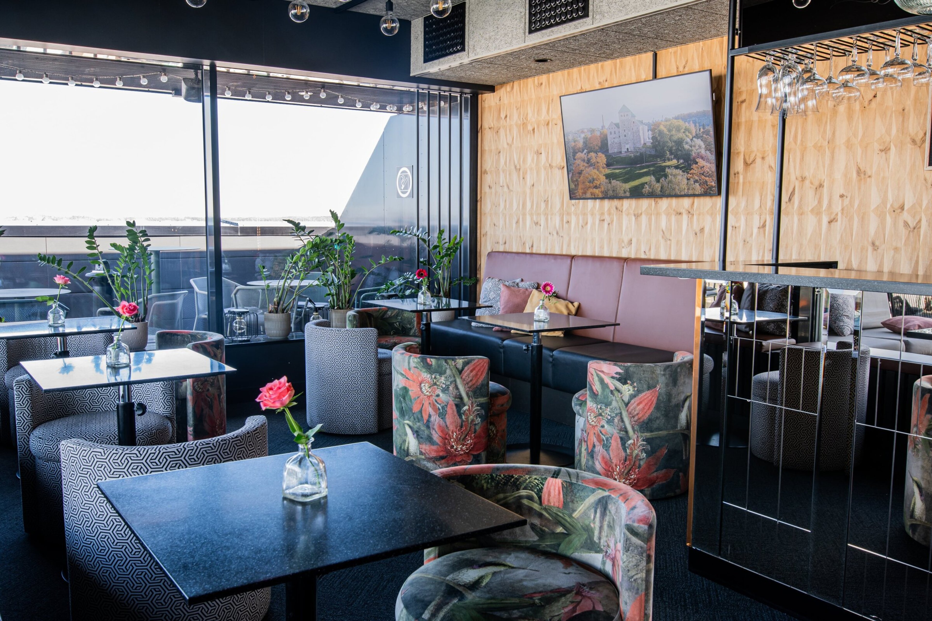 Kuppis Rooftop Bar, jossa värikkäitä tuoleja, kasveja ja suuret ikkunat terassille.