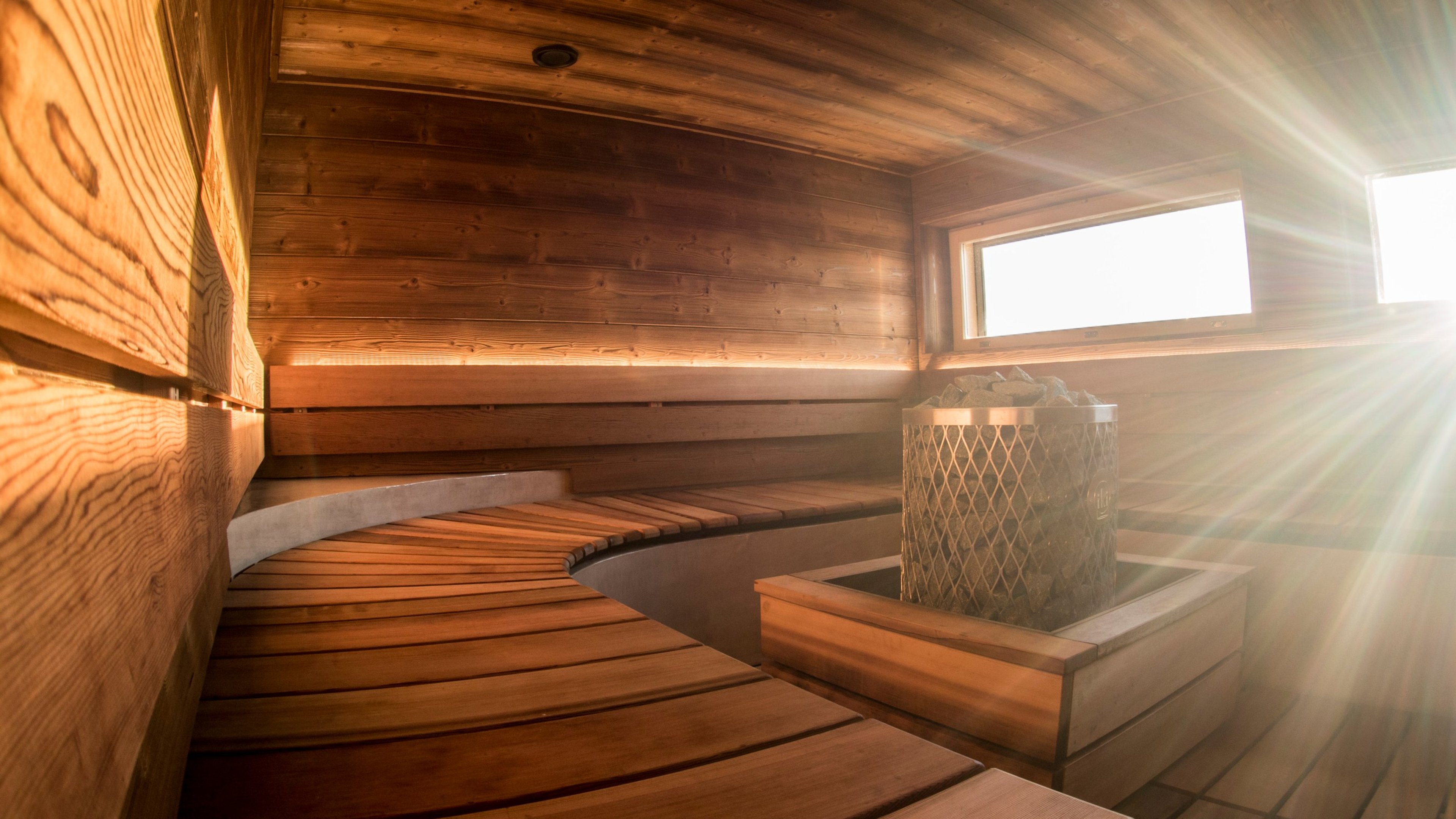 Modernin saunan sisätila puisilla lauteilla ja kiukaalla. Ikkunasta tulvii valoa lämpimään puupaneloituun tilaan.
