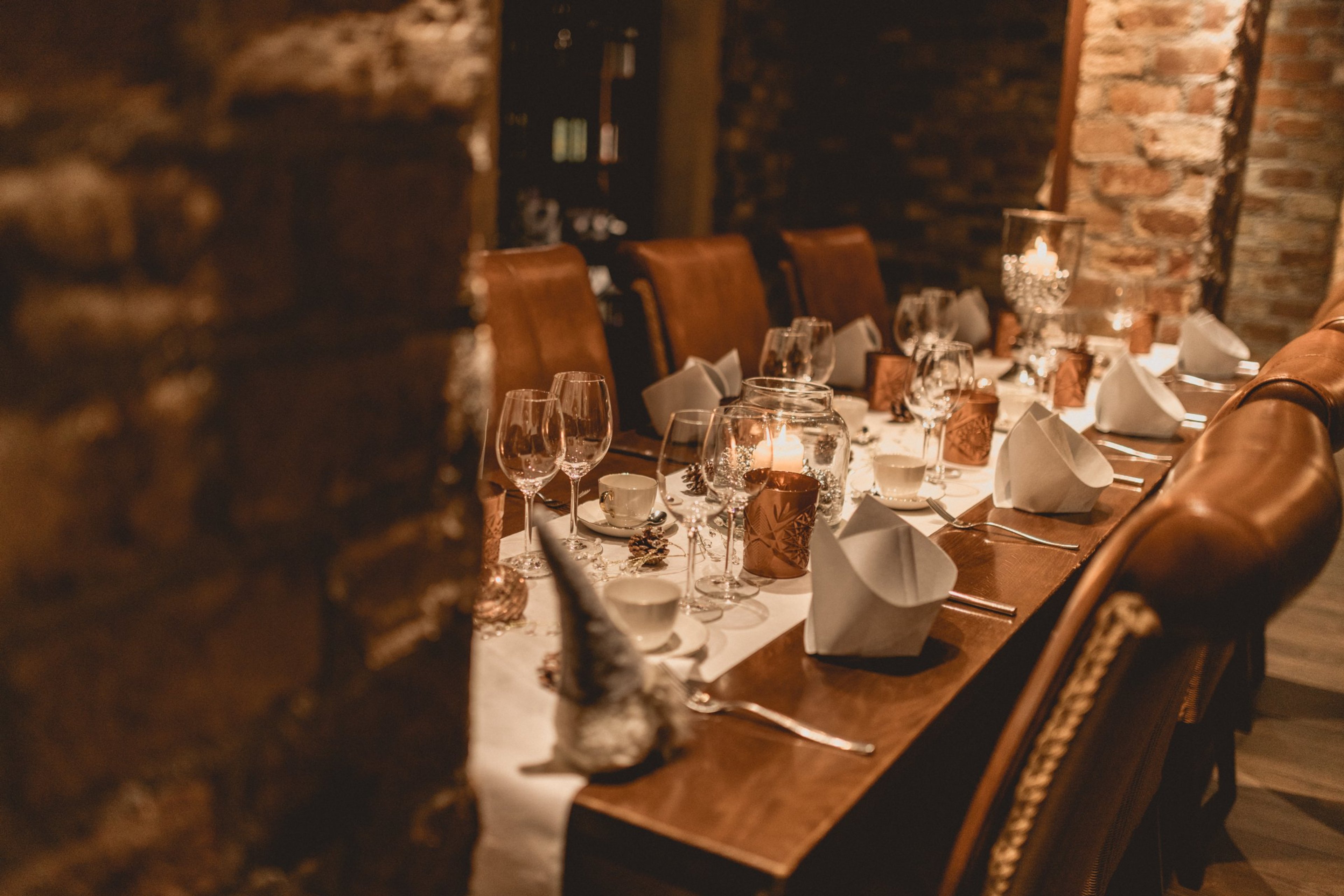Tunnelmallinen ravintolan pöytä kynttilöillä ja viinilaseilla, taustalla tiilivuoratut seinät ja nahkaiset tuolit.
