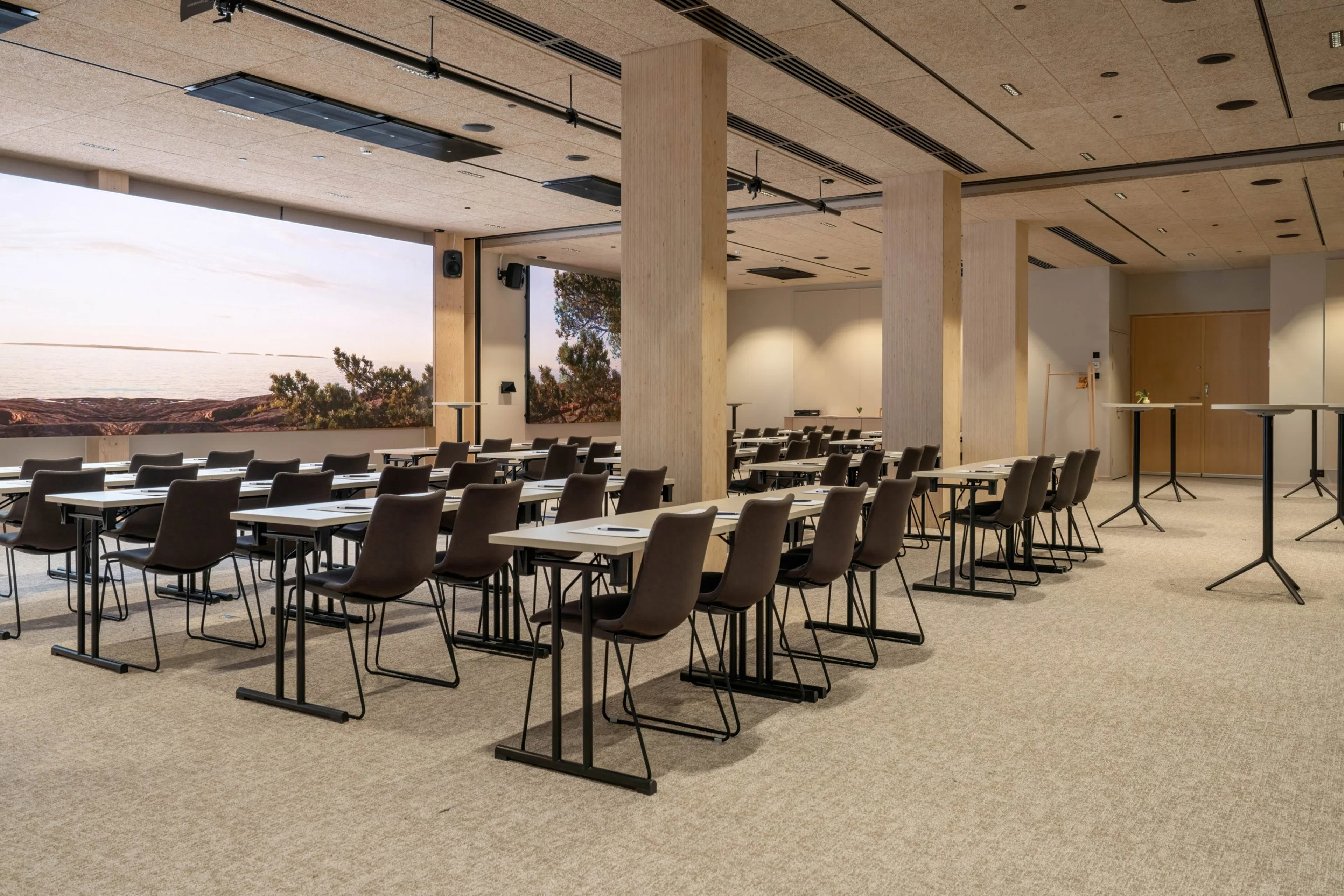 Modernt konferensrum med bord och stolar, naturligt ljus från fönster, jämn heltäckningsmatta och gott om utrymme att röra sig.