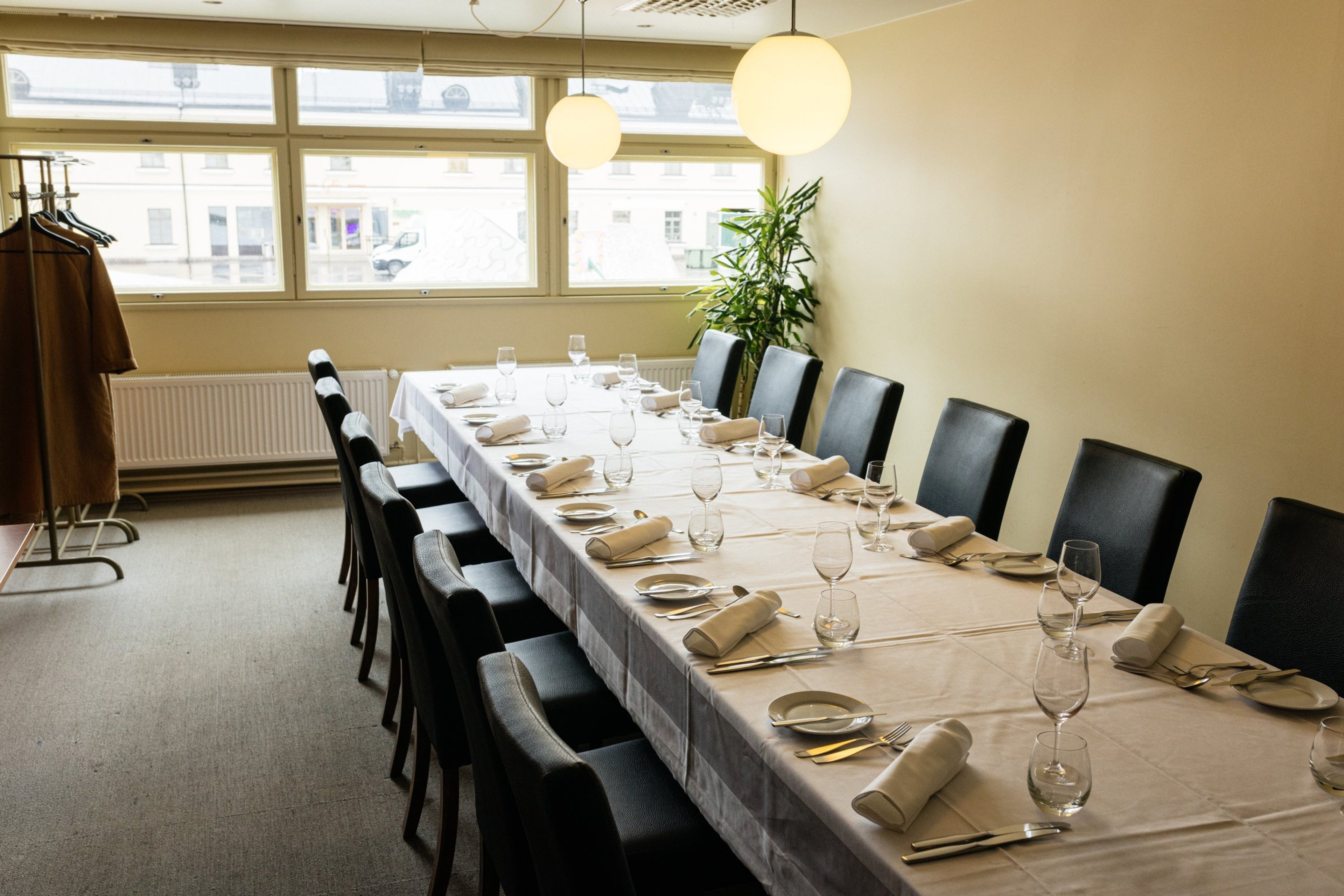 Ett långt matbord dukat i ett privat rum. Med vit duk, svarta stolar. Rummet är ljust tack vare stora fönster.