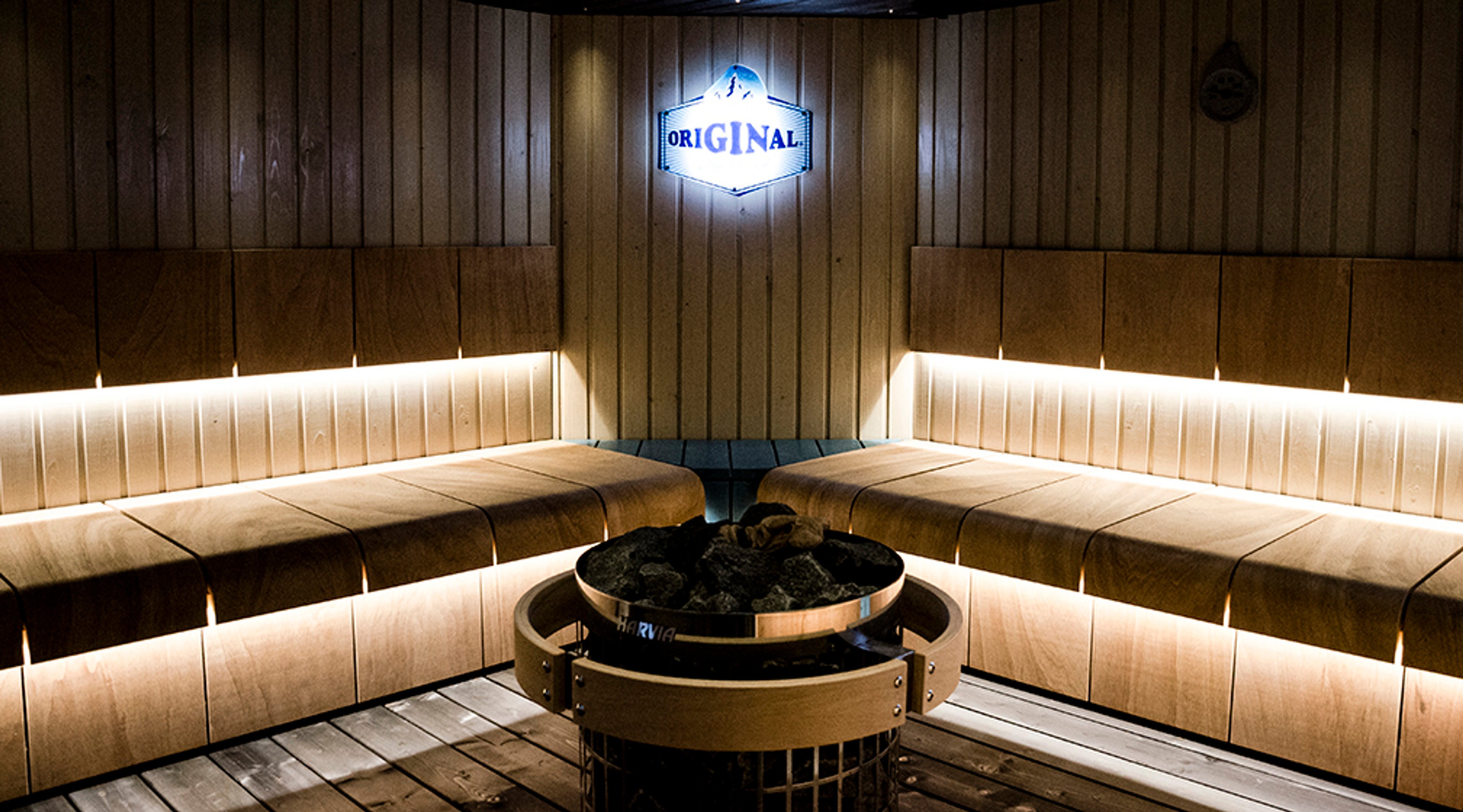 Moderni sauna puupaneeliseinillä, tunnelmavalaistuksella ja keskellä kiviä sisältävä kiuas.