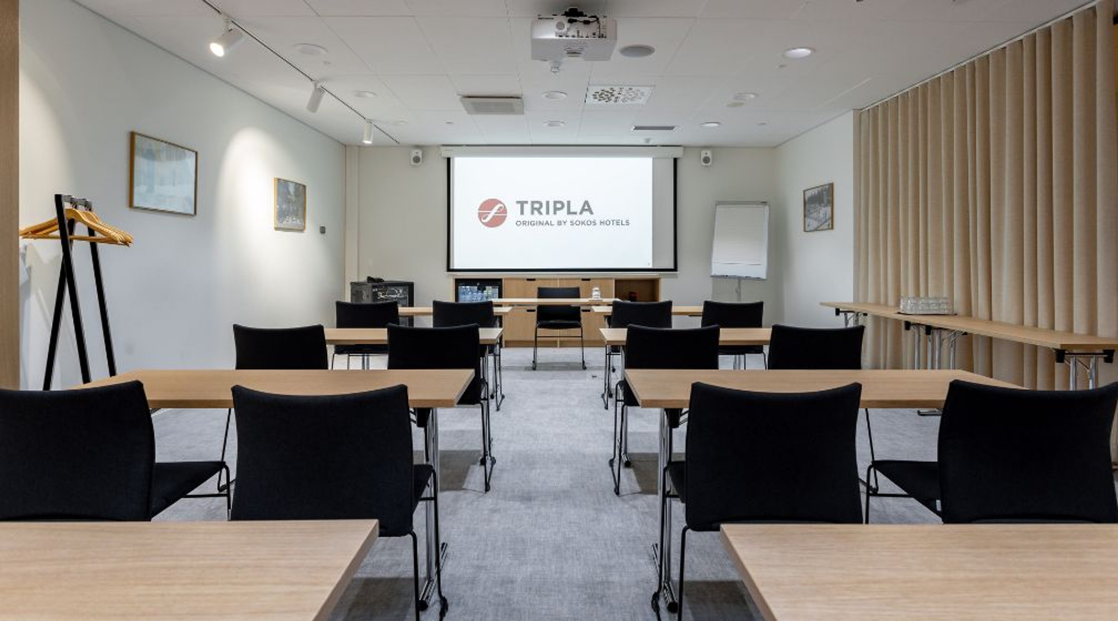 Modernt mötesrum med träbord, svarta stolar och vit projektorskärm. Jämnt golv, god belysning.