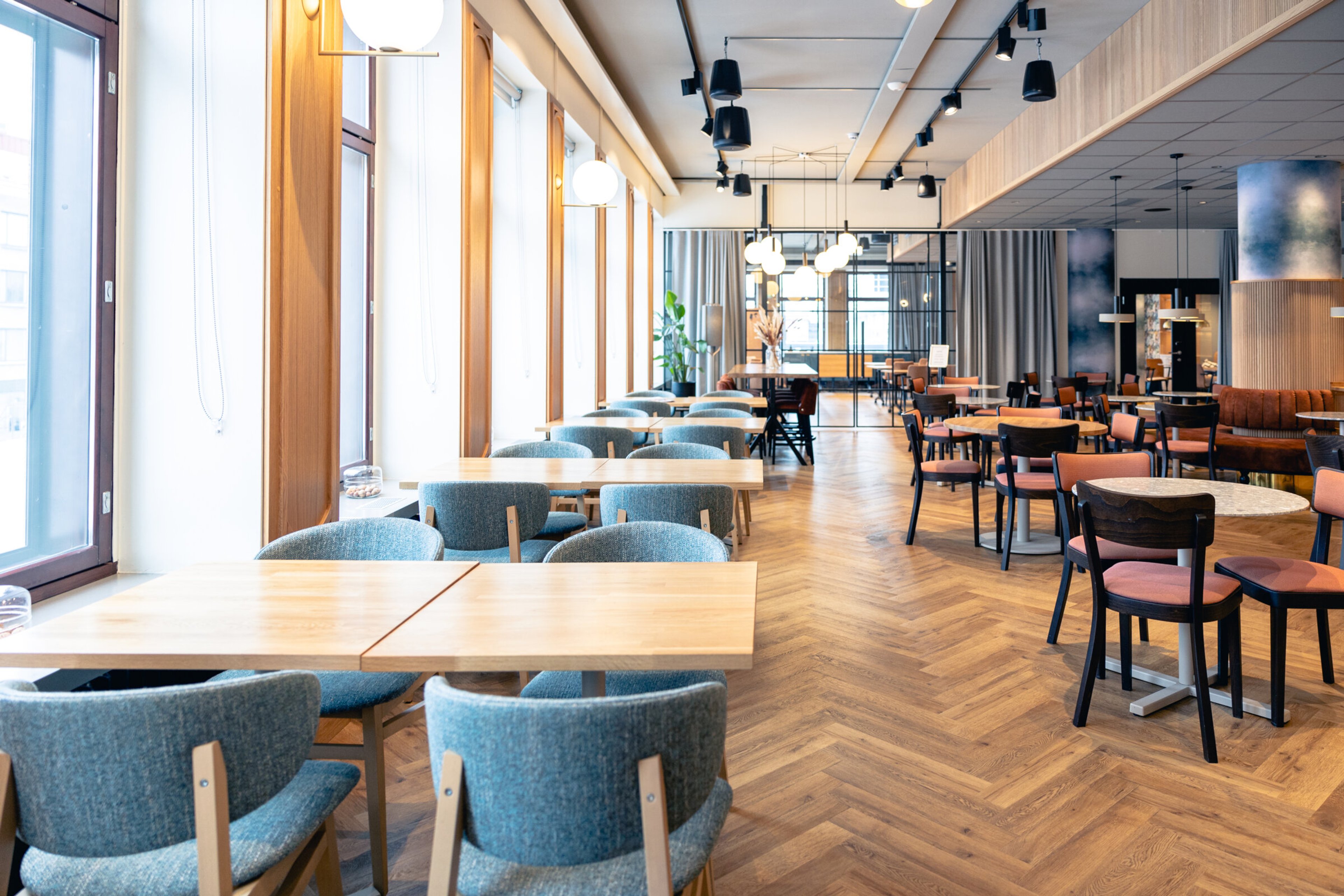 Rymlig restaurang eller matsal med glasdörrar och jämnt parkettgolv. Lokalen har matgrupper med stolar i olika färger.