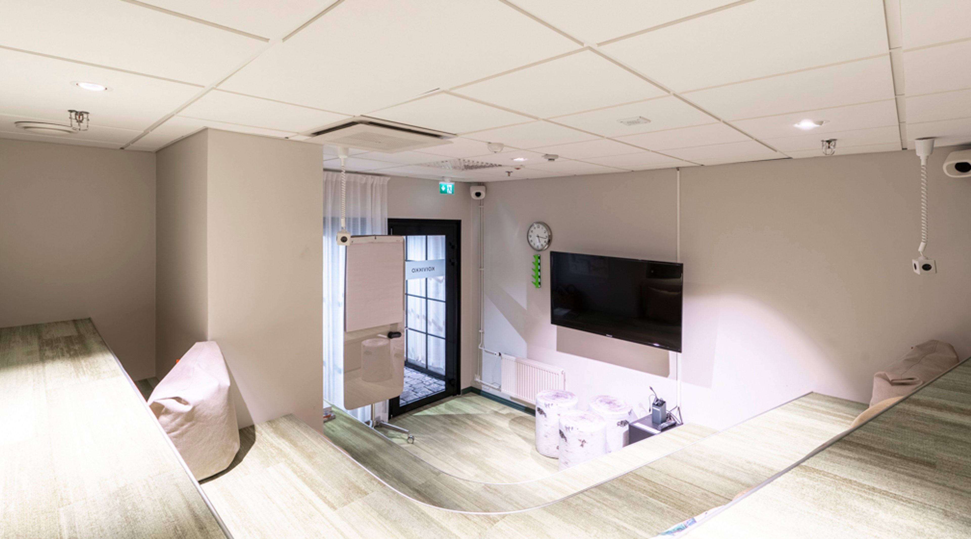 Neuvotteluhuone, jossa on vaaleanharmaat seinät, vaalea lattia, televisio seinällä, valkotaulu ja lasinen uloskäynti.