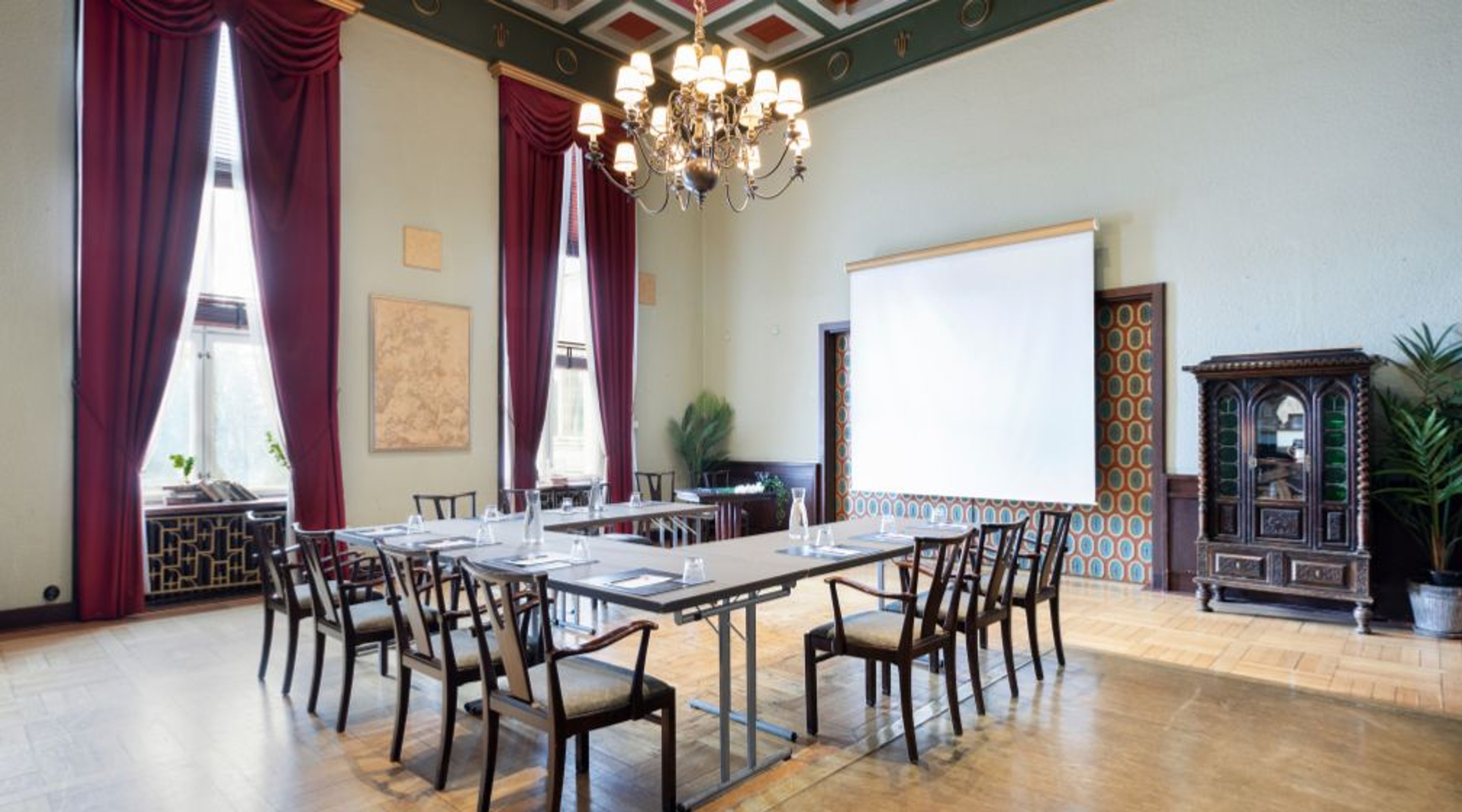 High-ceilinged meeting room with hard floor surface, natural lighting from tall windows and large chandelier.