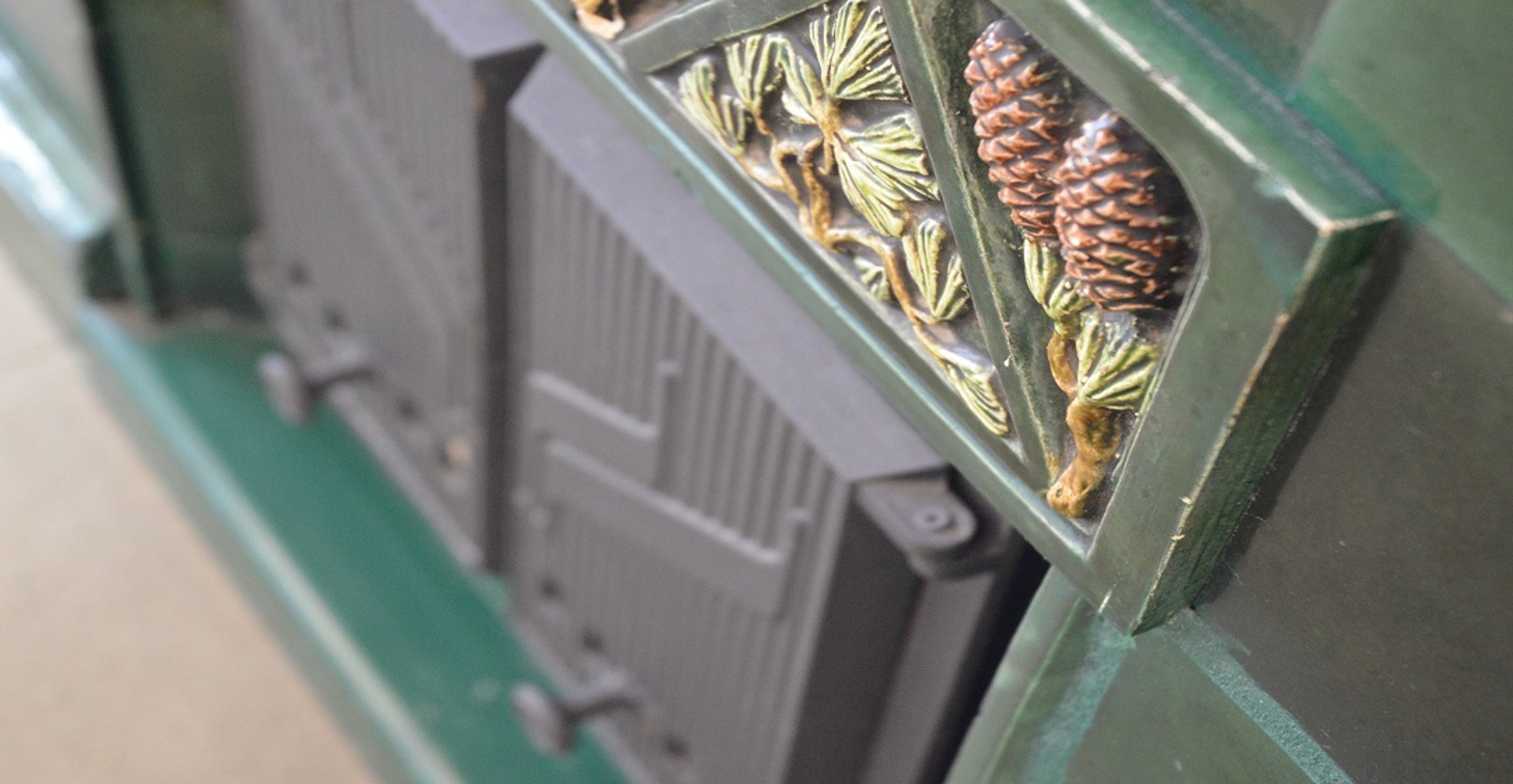 Vihreän kaakeliuunin koristeellinen paneeli, jossa on käpyjä ja kasviaiheita.