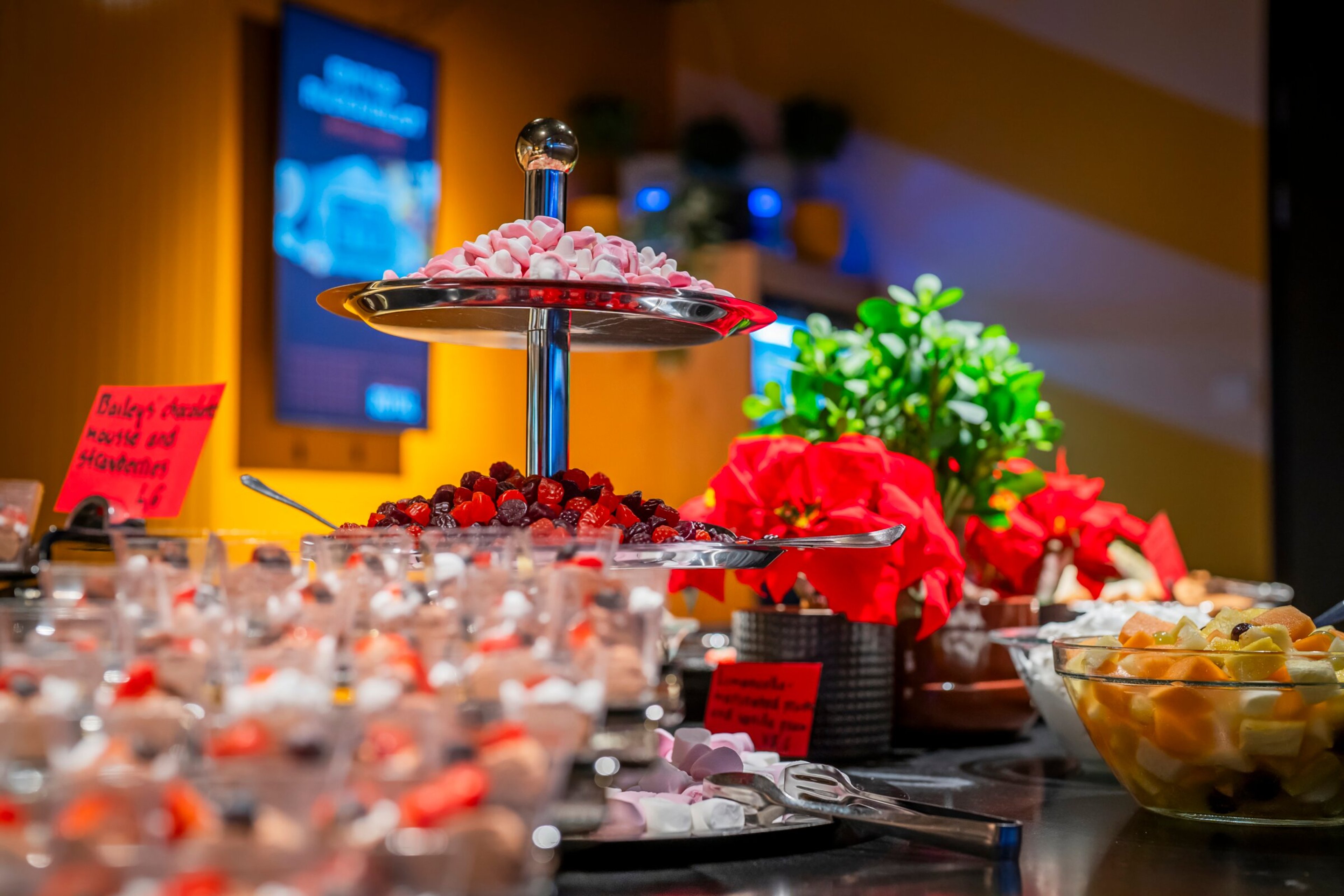 Juhlapöydän herkkuja sisältäen kakkuteline makeisilla, marjoja, jälkiruokia laseissa ja punaisia joulutähtiä koristeena.