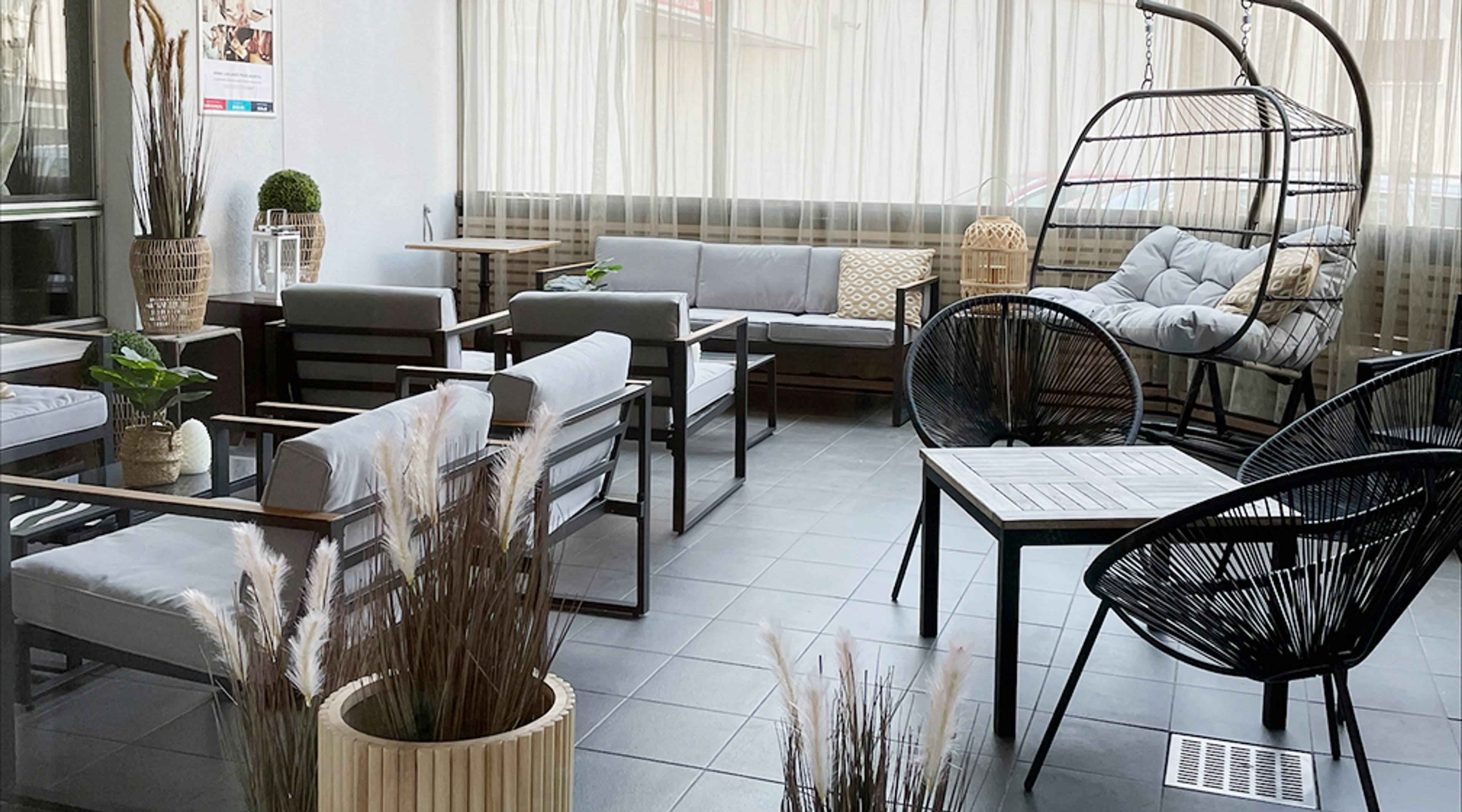 Moderni oleskelutila harmailla sohvilla, mustilla tuoleilla ja riippuvalla keinutuolilla. Tilassa on tasainen laattalattia ja suuret ikkunat.