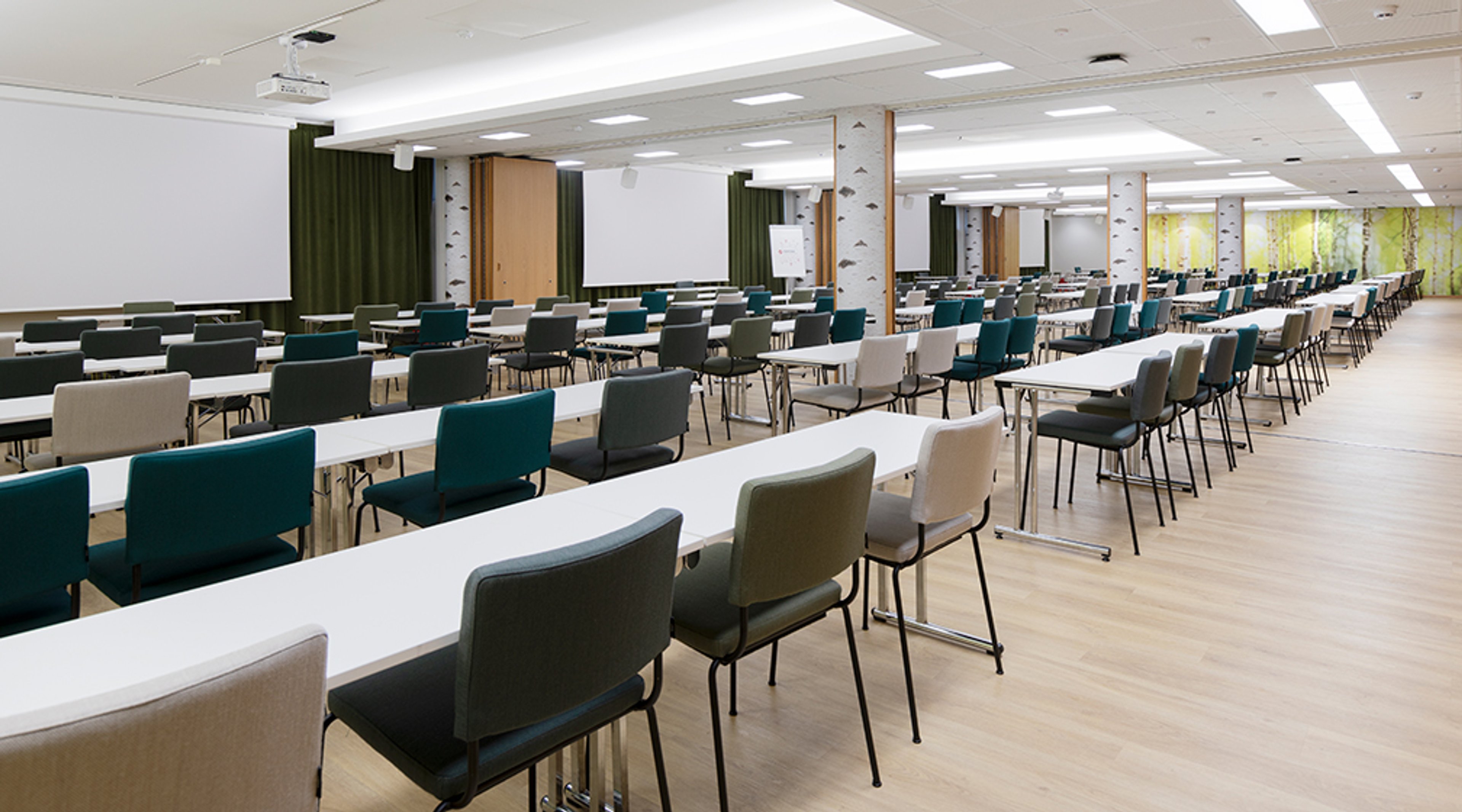 Modern conference room with long white tables and blue and grey chairs. The room features a projector screen and wooden flooring.
