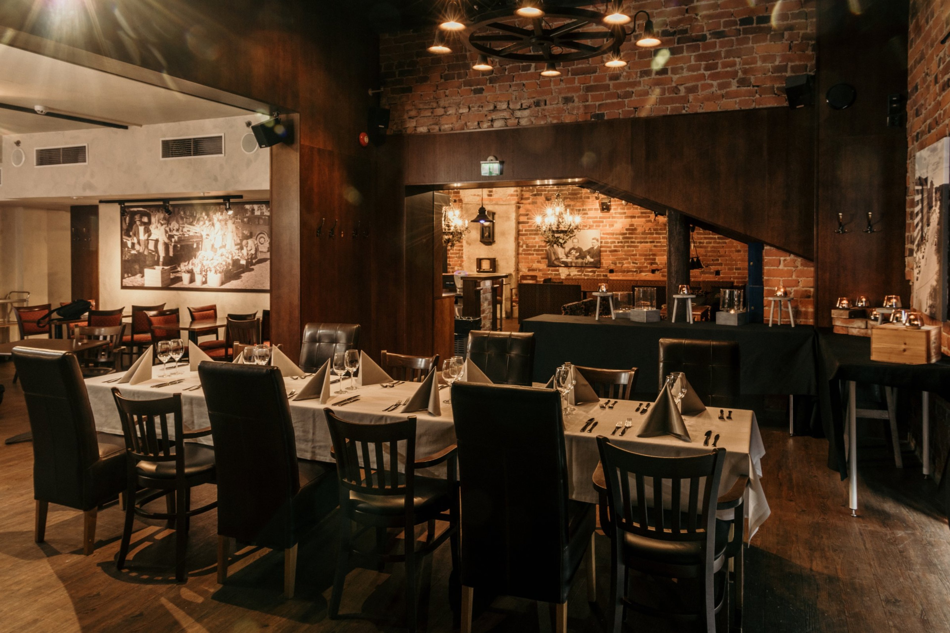 Tunnelmallinen ravintolan sisätila, jossa tiiliseinät, puulattia ja kattokruunu. Useita pöytiä valmiina ruokailijoille.