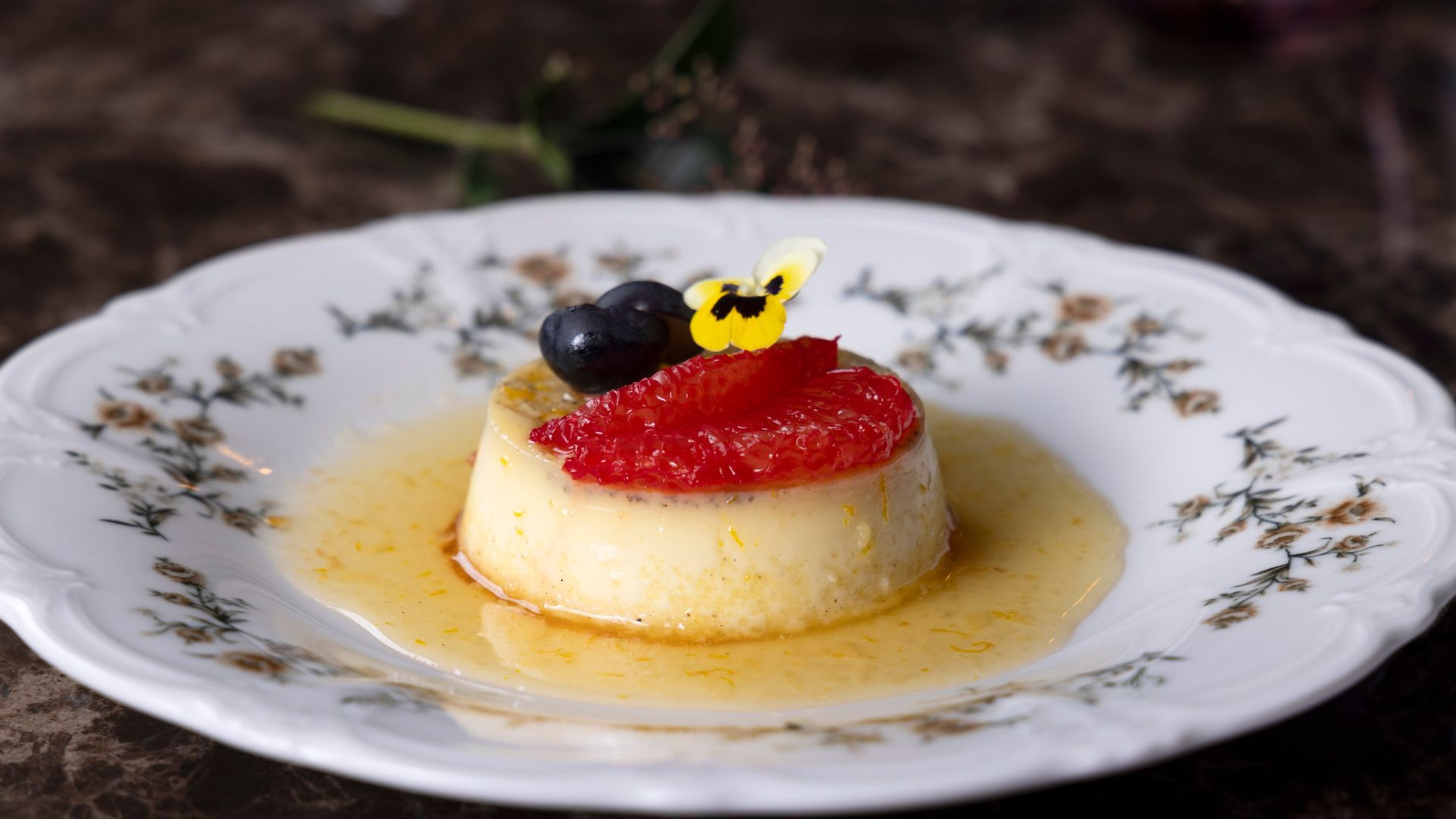 Pannacotta jälkiruoka koristeellisella posliinilautasella, päällä mansikkaa, mustikka ja keltainen syötävä kukka kevyessä kastikkeessa.
