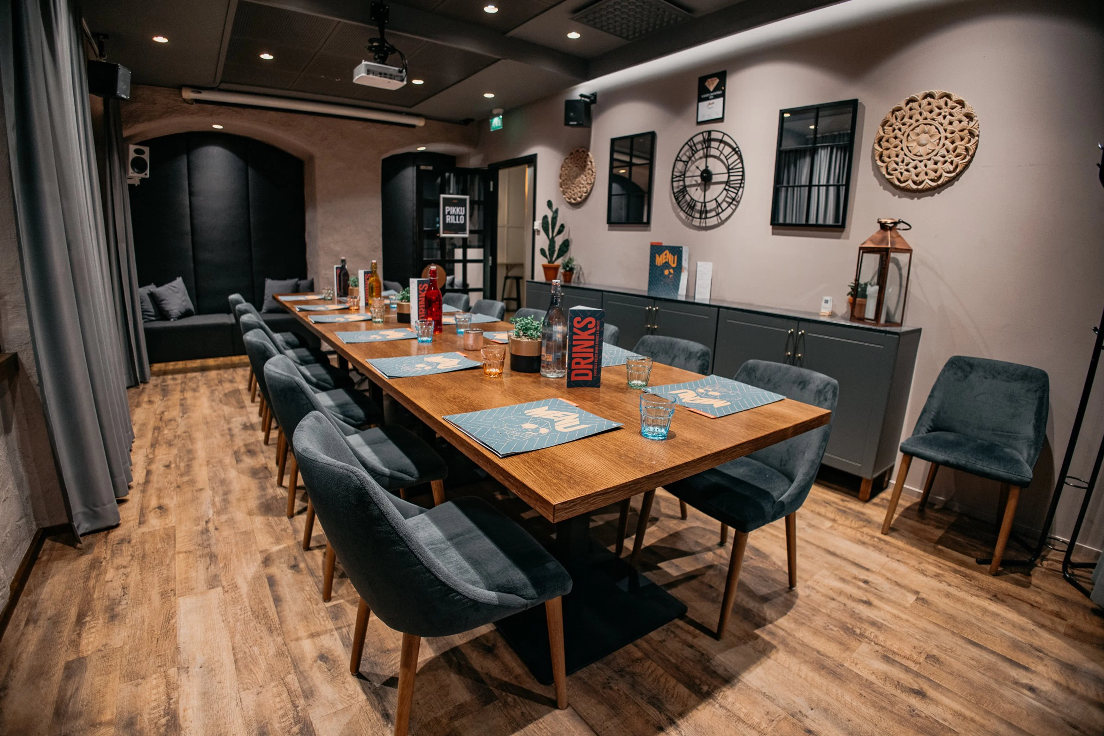 Tyylikäs kokoustila, jossa pitkä puupöytä sinisillä tableteilla, tummanharmaita nojatuoleja ja puinen lattia. Seinillä kelloja ja koriste-esineitä.