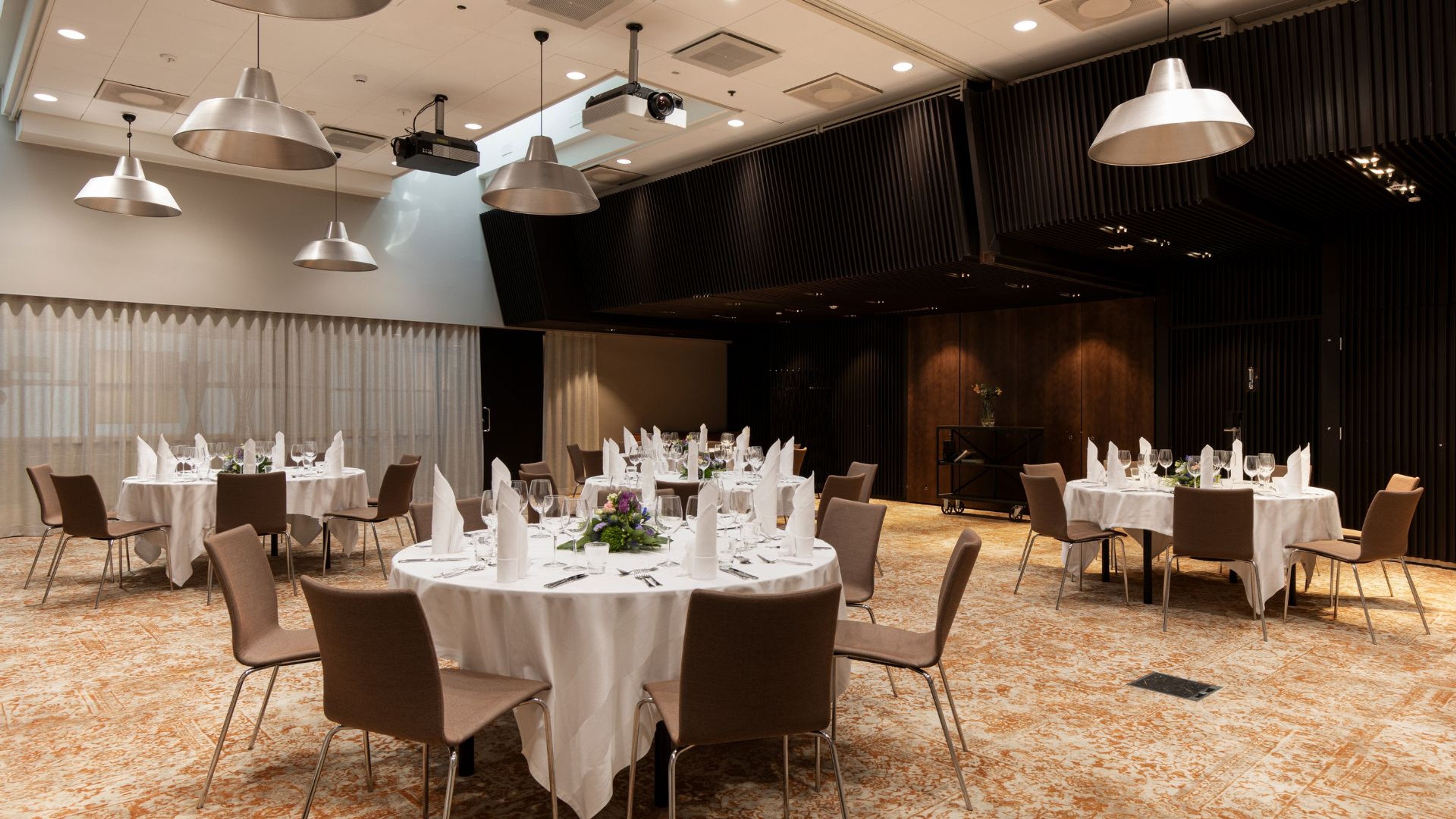 Juhlatila pyöreillä pöydillä, valkoisilla liinoilla ja serveteillä. Tasainen lattia, hyvä valaistus ja esteetön tila.