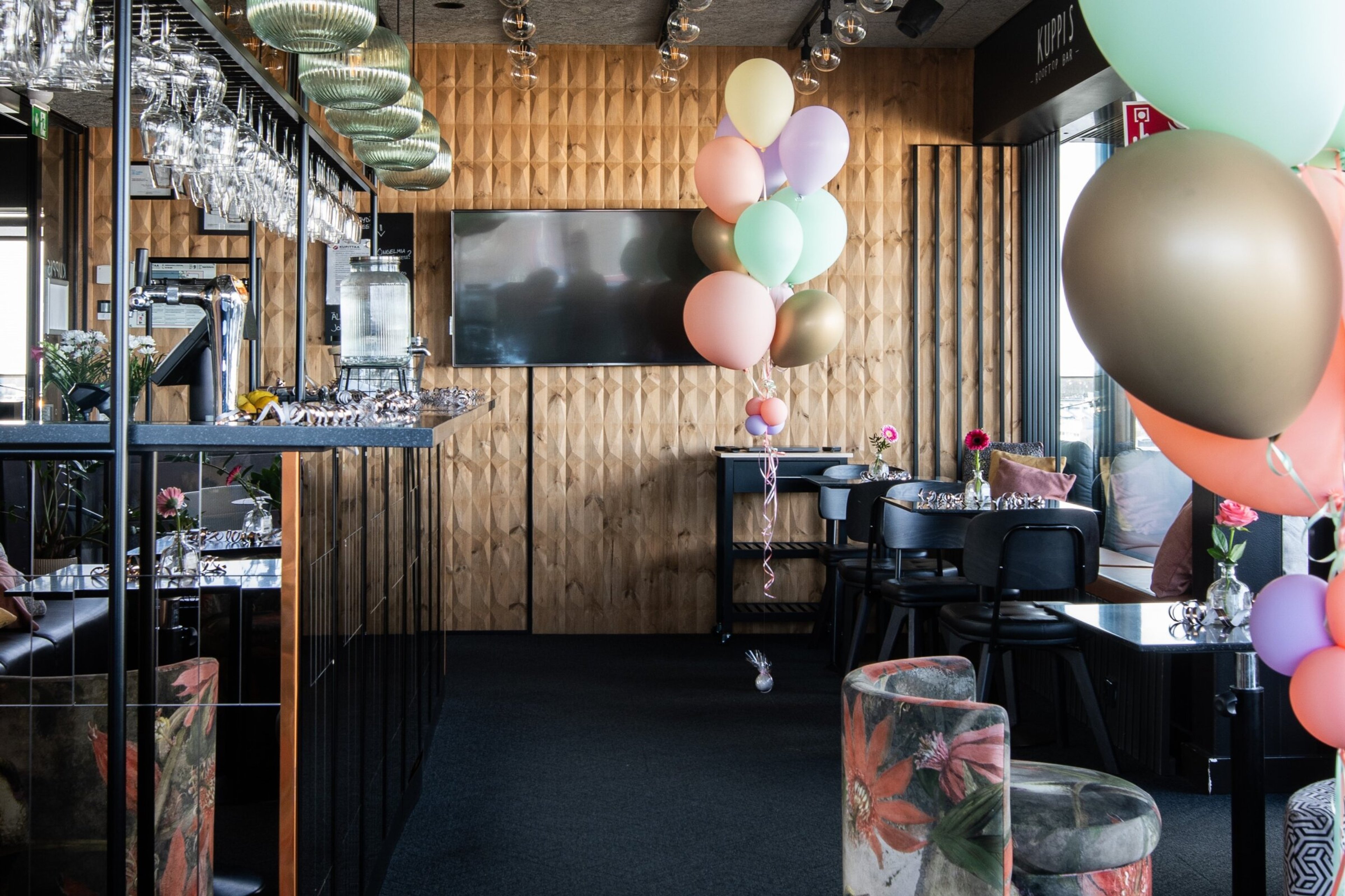 Juhlakoristeltu Kuppis Rooftop Bar, jossa baaritiski vasemmalla ja pöytiä oikealla. Ilmapalloja koristeena.