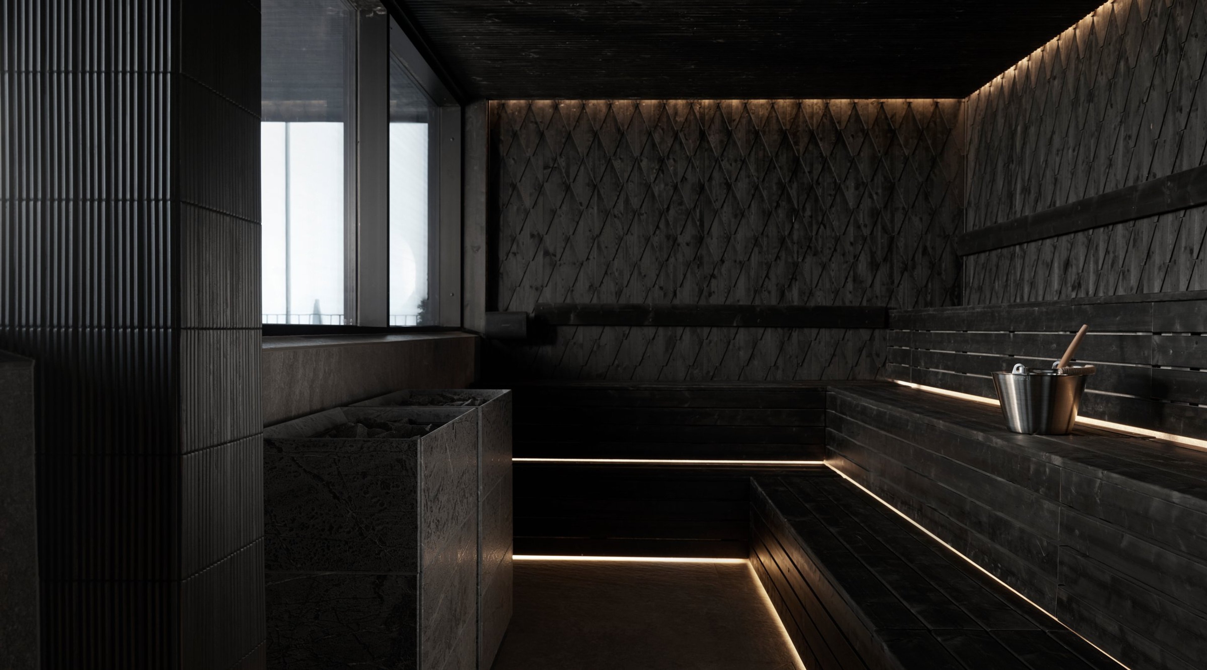 Moderni tumma sauna tyylikkäällä valaistuksella, puiset istuintasot ja metallinen saunaämpäri kauhalla.