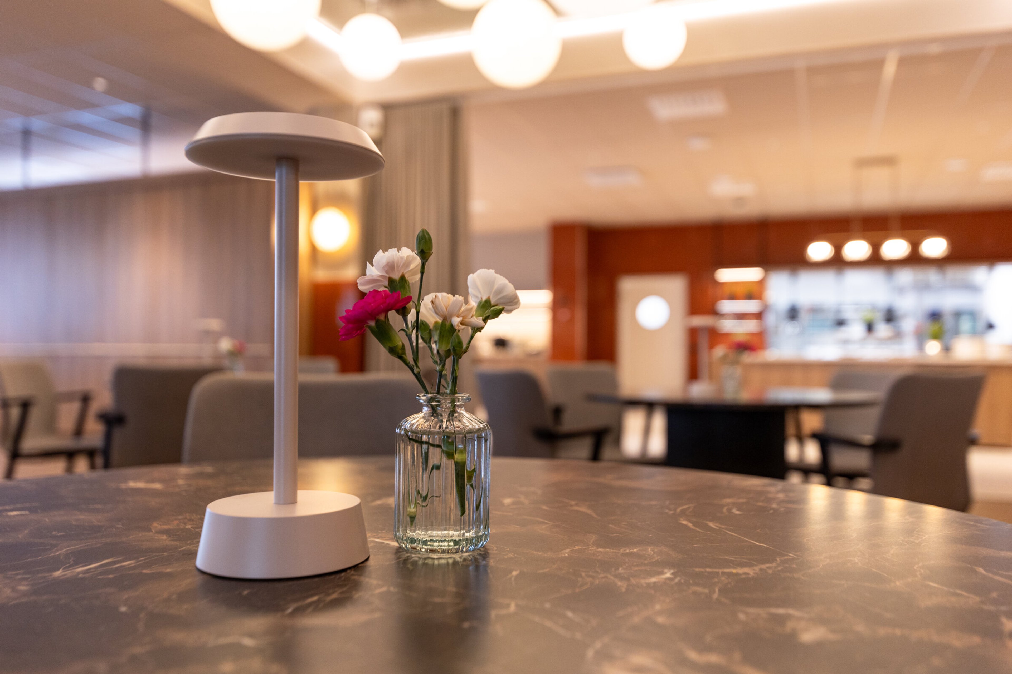 Moderni lounge-tila, jossa pöytiä ja matalia istuimia. Pöydät ovat eri korkeuksilla, taustavalaistus on hämärä.