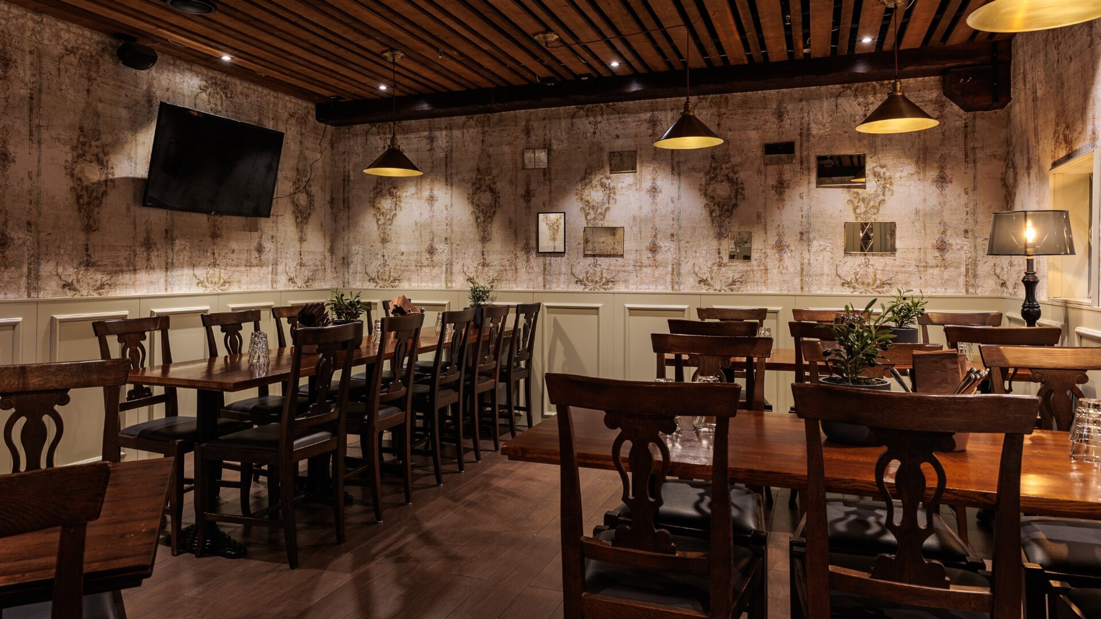 Ravintolan sisätila jossa tummia puisia pöytiä, riippuvia valaisimia, puinen kattopanelointi ja koristeellinen tapetti. Hardwood-lattia, tasainen pinta.