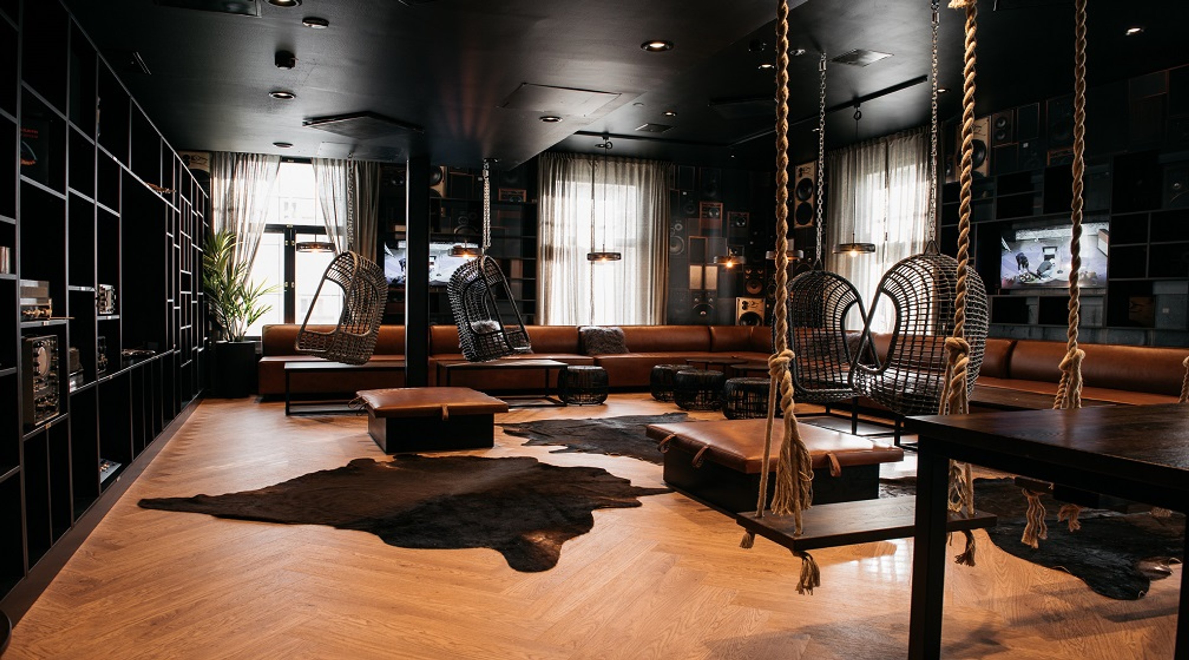 Tyylikäs lounge-tila mustilla seinillä, puulattialla ja roikkuvilla rottinkituoleilla. Huoneessa oransseja sohvia ja eläintalja mattoja.