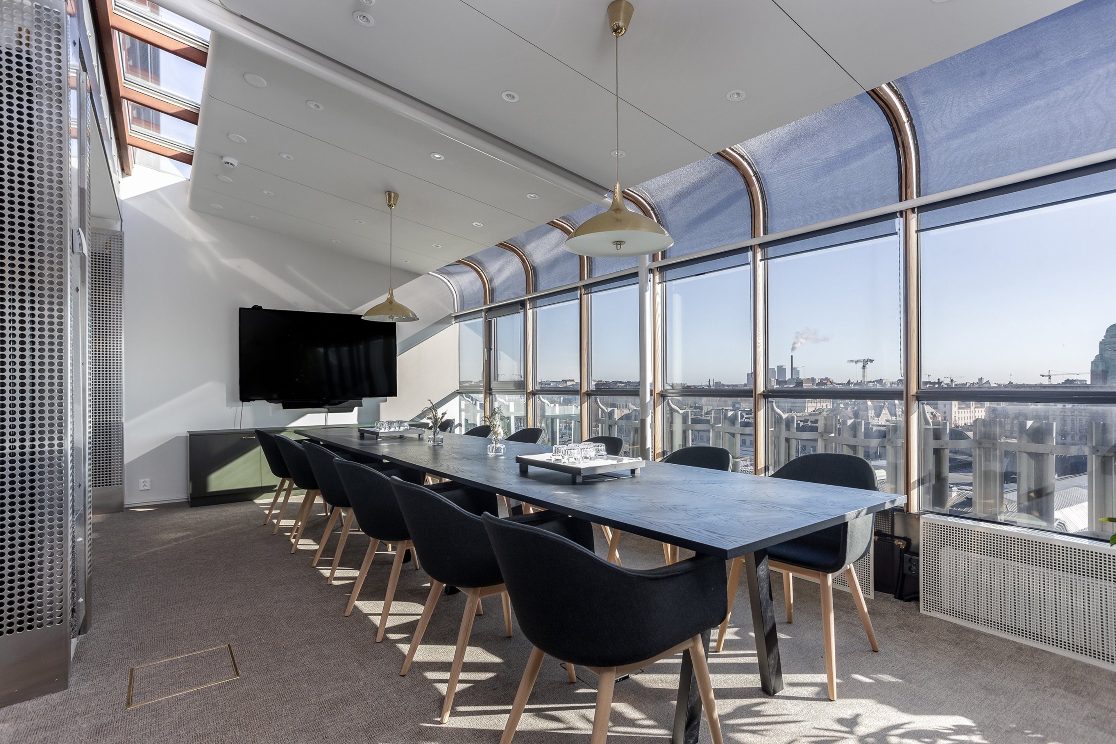 Modernt konferensrum med långt svart bord, svarta stolar och stora fönster med stadsutsikt. Rummet har väggmonterad TV och jämnt golv.