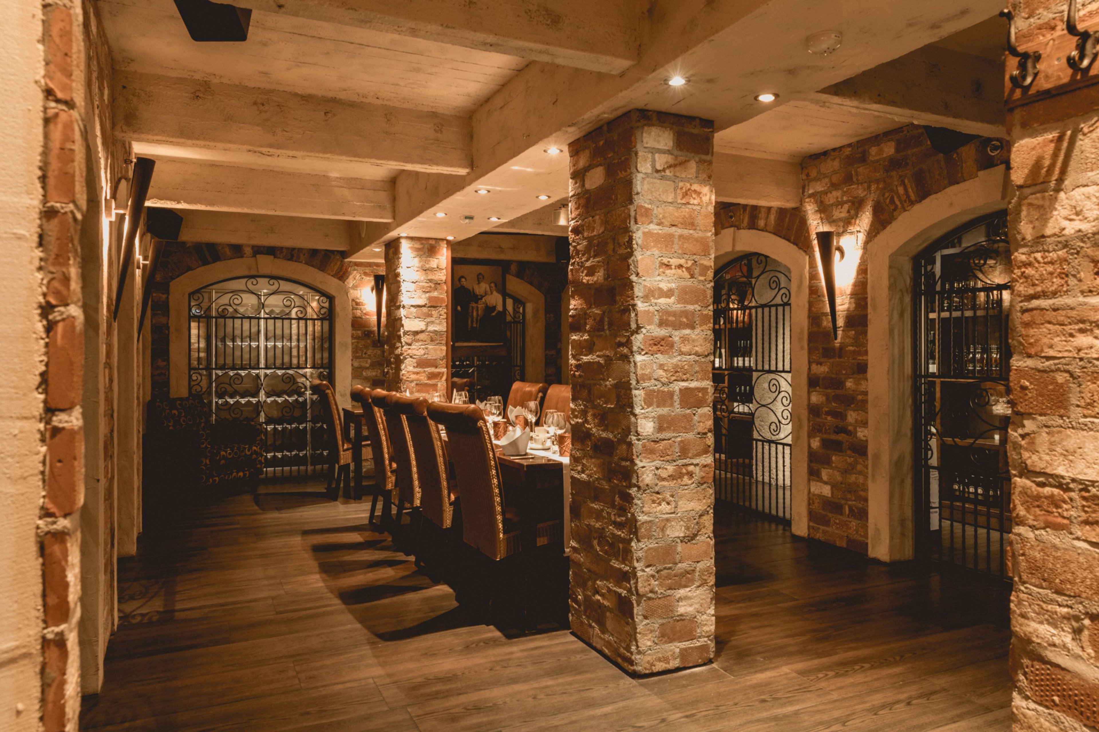 Tunnelmallinen ravintolan sisätila tiilipilareilla, kaarevilla holviaukoilla ja rautaporteilla. Lattialla kova puupinta, hämärä valaistus.
