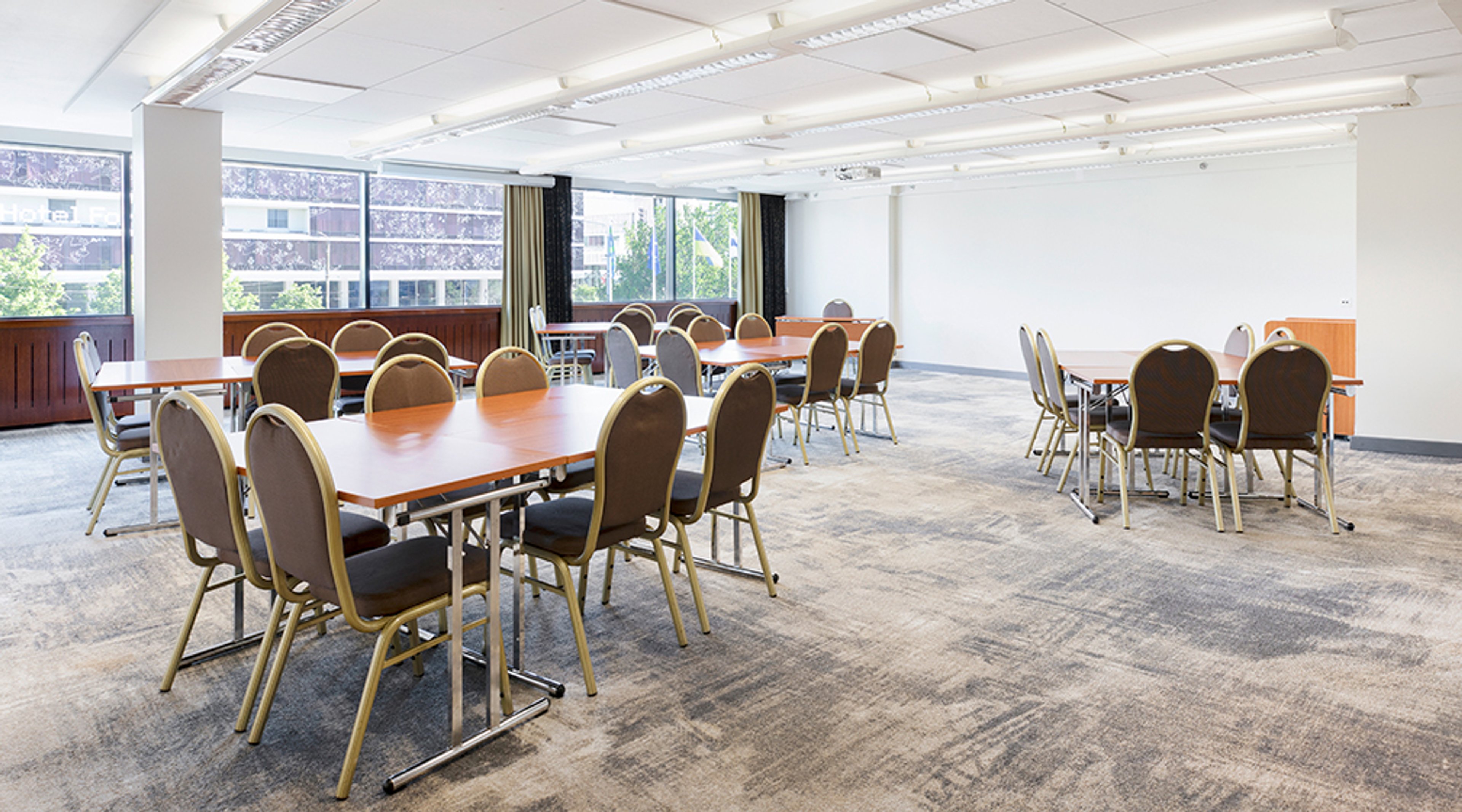 Bright meeting room with multiple tables and chairs, level flooring with low-pile carpet.