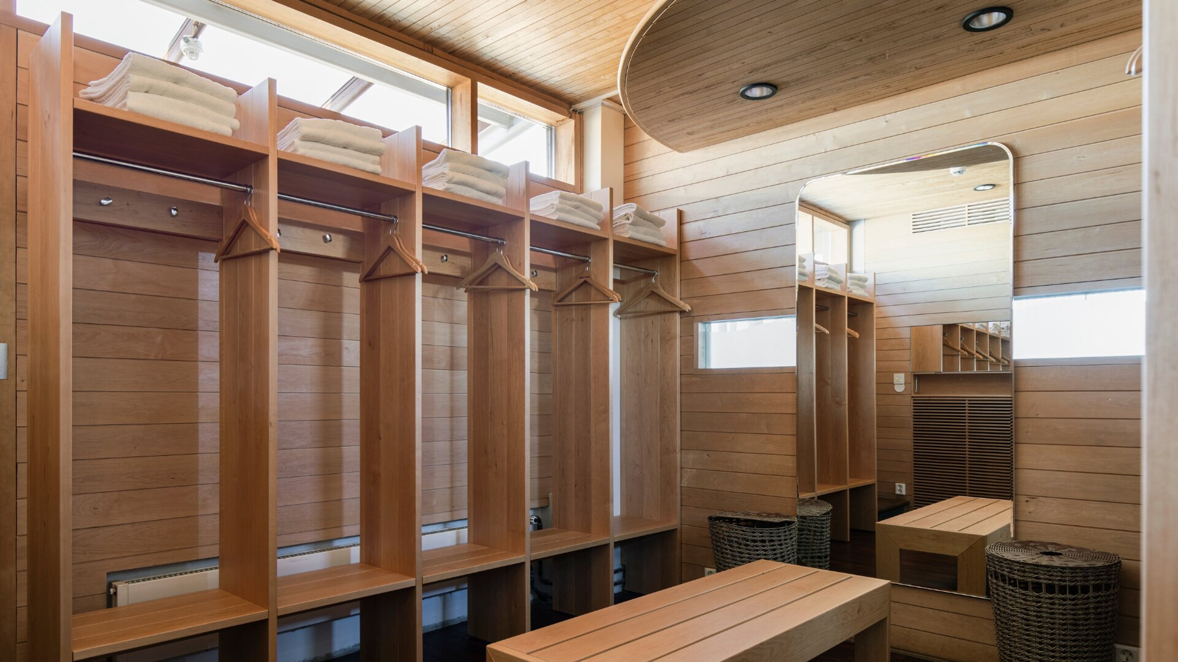 Puupaneloitu pukuhuone, jossa on rivissä vaatteille naulakot, yläosassa hylly pyyhkeille ja penkkejä istumista varten.