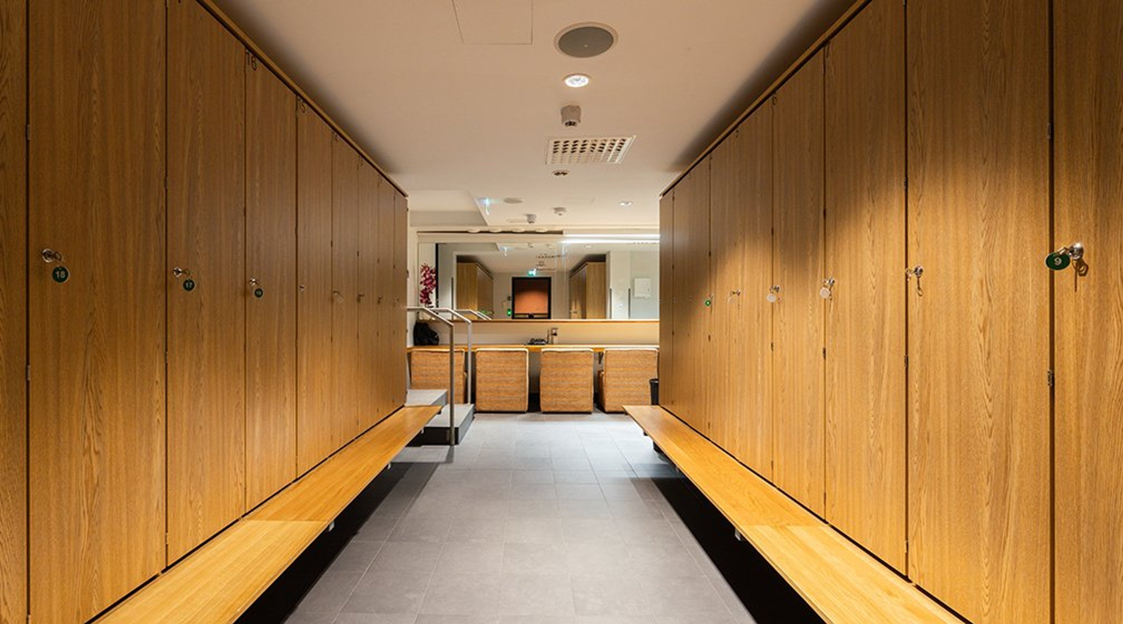 Modernin pukuhuoneen sisätila puisilla kaapeilla ja penkeillä. Tasainen kivinen lattia, selkeä valaistus ja leveä käytävä.