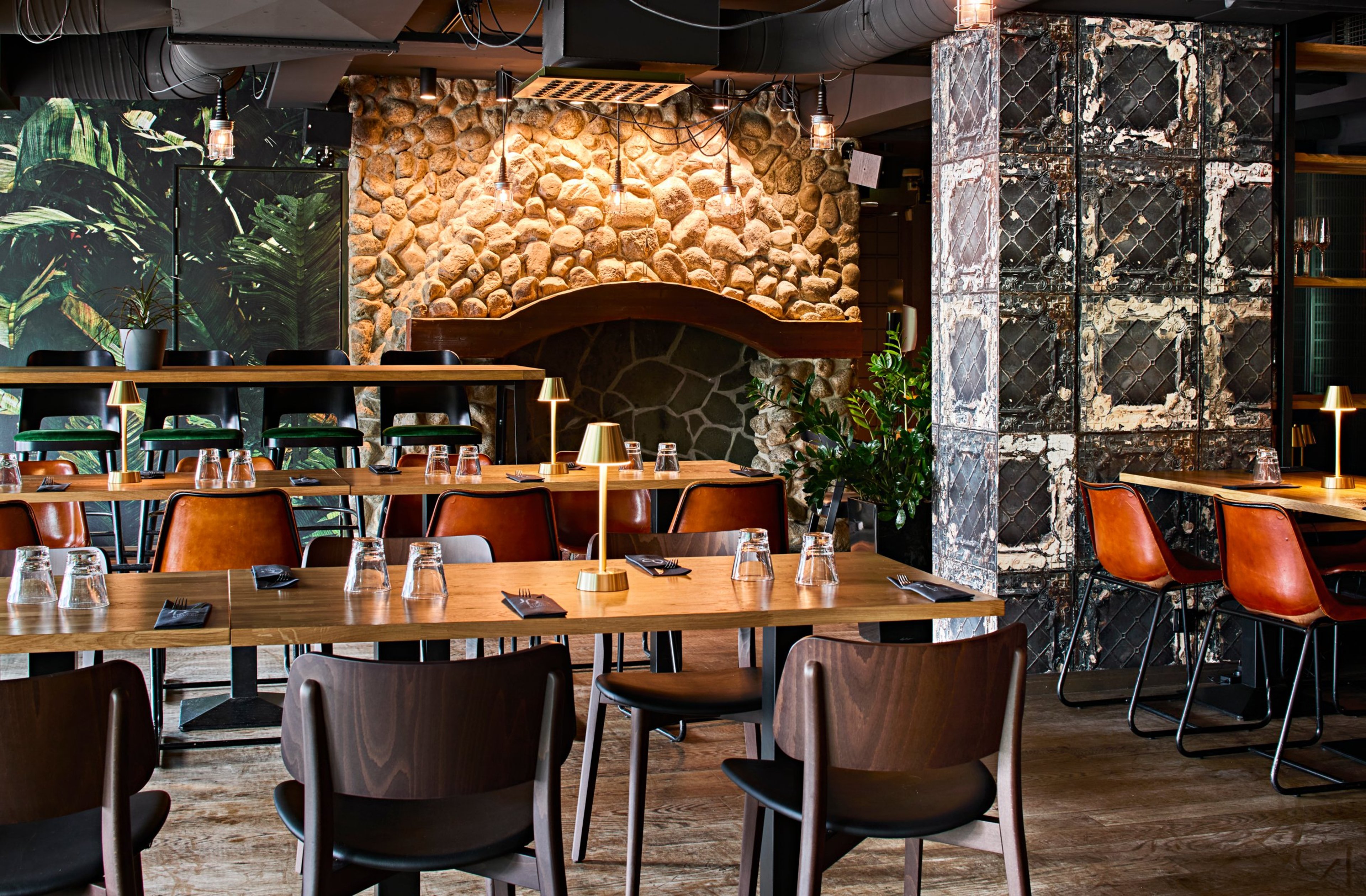 Moderni ravintola kiviseinällä ja kasviseinäteemalla. Puupöydät, nahkaiset tuolit, tasainen puulattia ja riittävästi tilaa pöytien välillä.