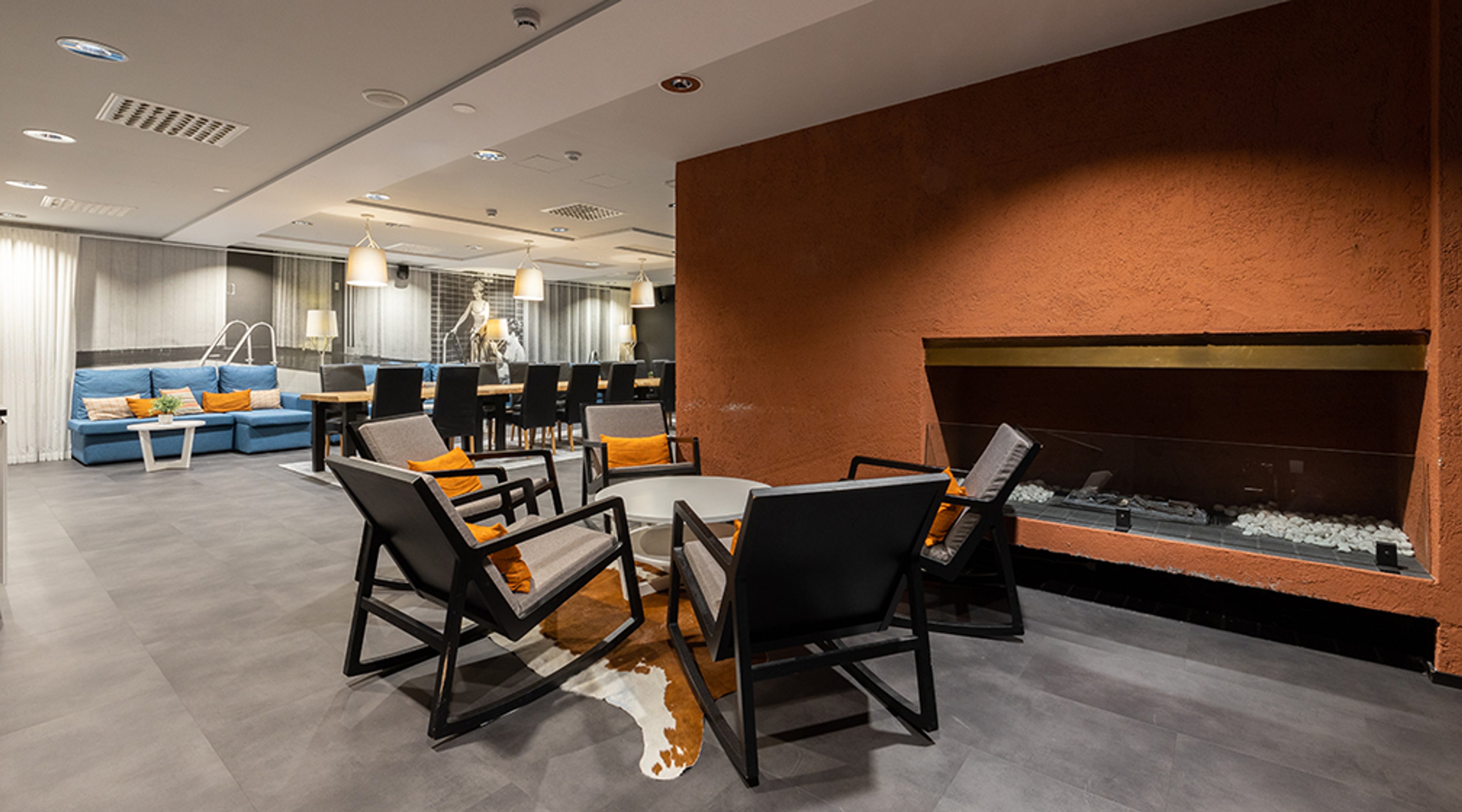 Moderni oleskelutila, jossa takkaseinä, mustia tuoleja oranssein tyynyin, sininen sohva ja ruokailupöytä.