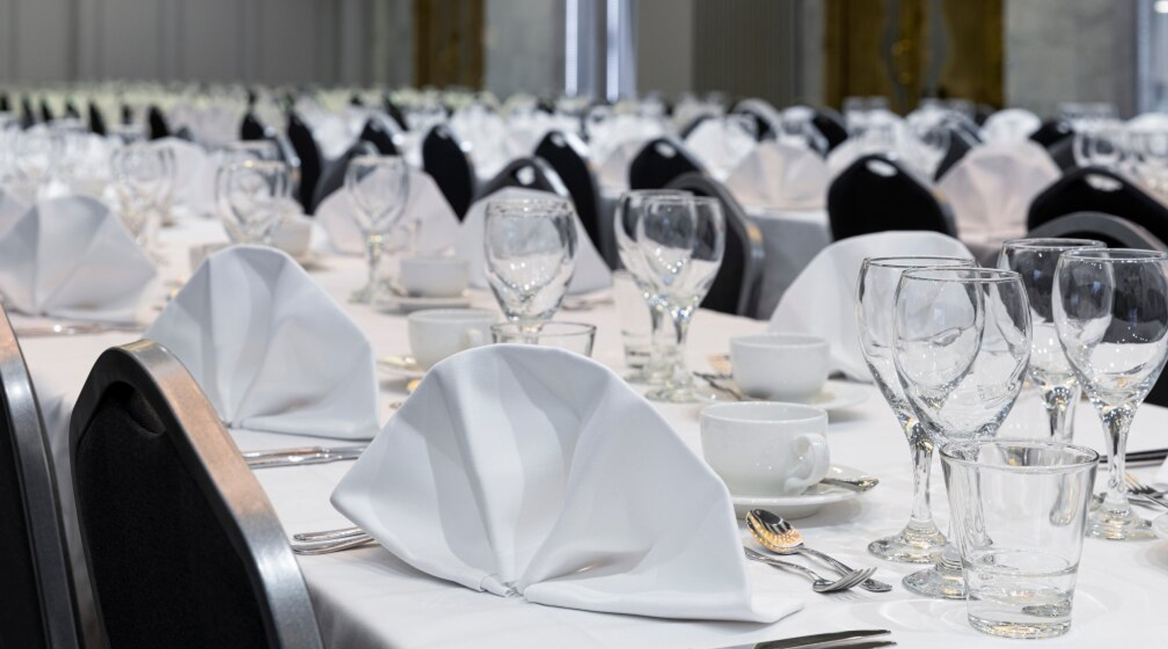 Juhlavasti katettu ruokasali mustilla tuoleilla ja valkoisilla pöytäliinoilla, lautasliinat taiteltu kauniisti.
