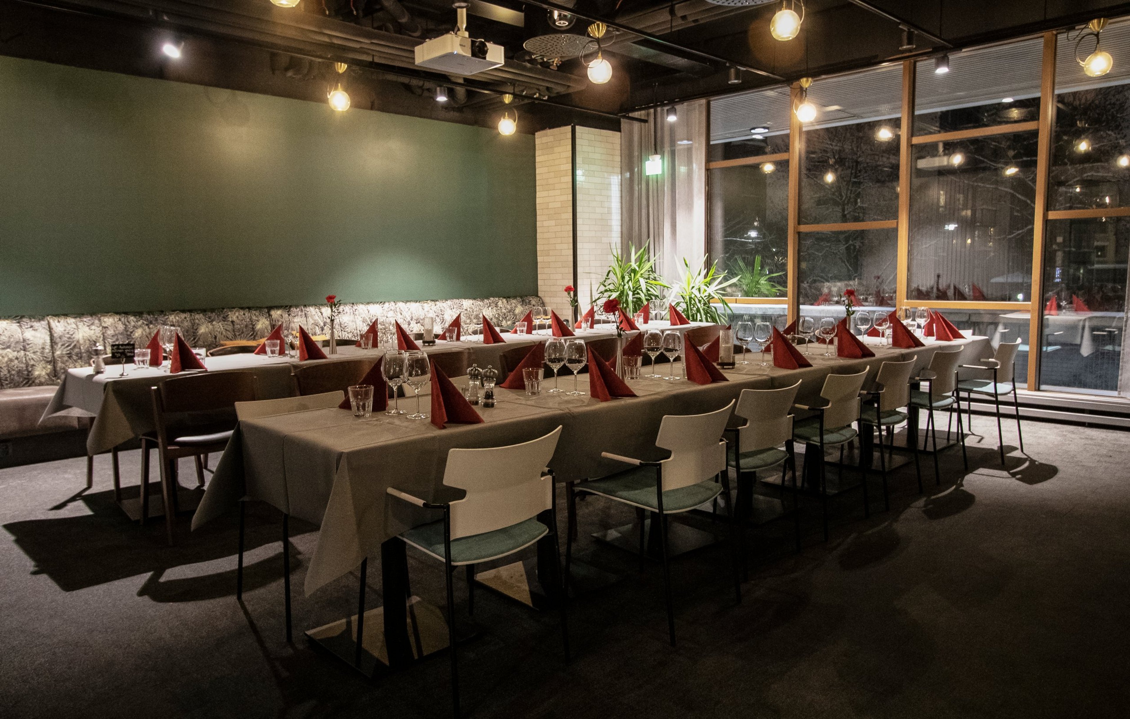 Ravintolan ruokasali, jossa vihreä seinä, sohvia ja suuret ikkunat. Tila on hyvin valaistu.