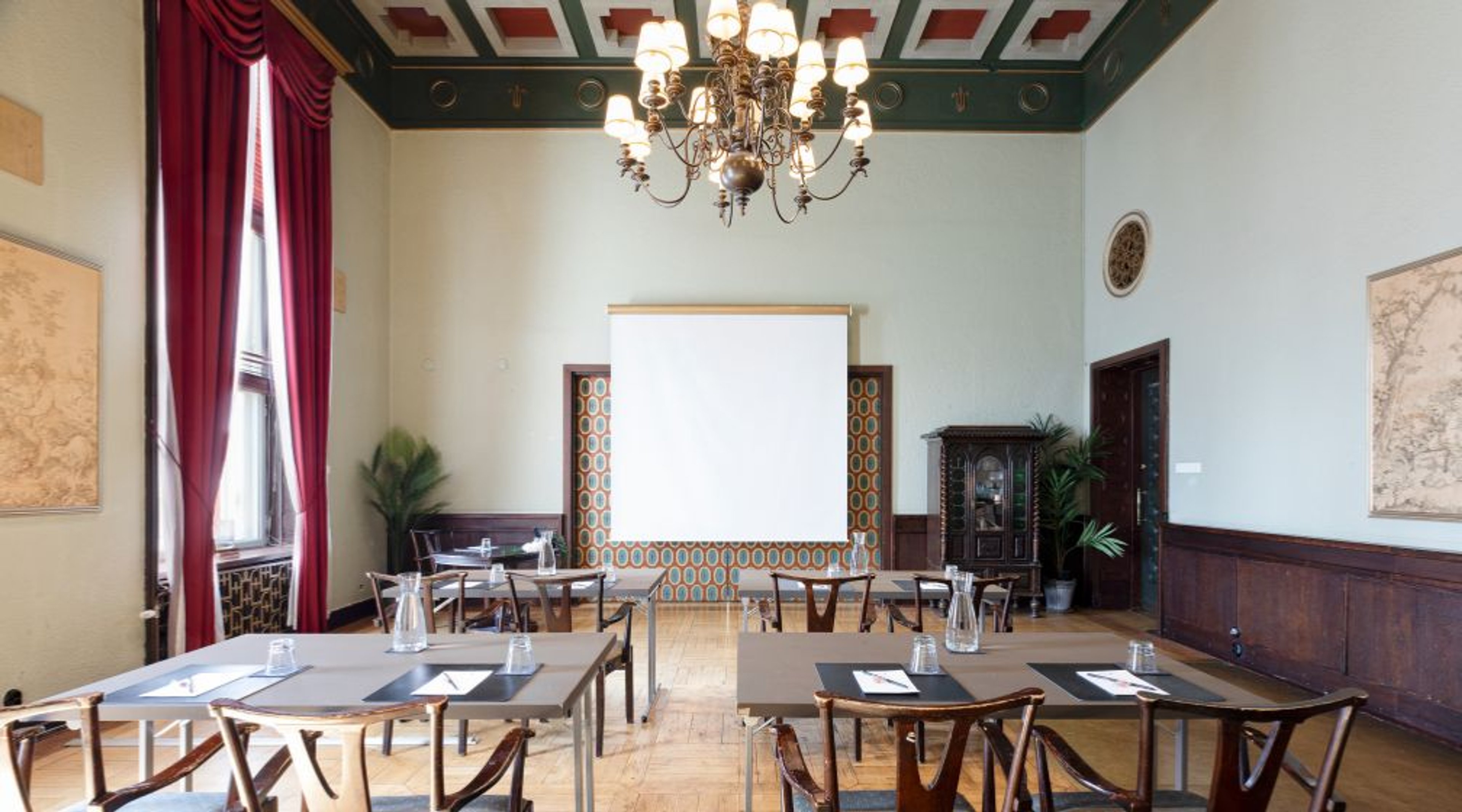 Conference room with high decorative ceiling, multiple tables and chairs, and light-colored hard parquet flooring.