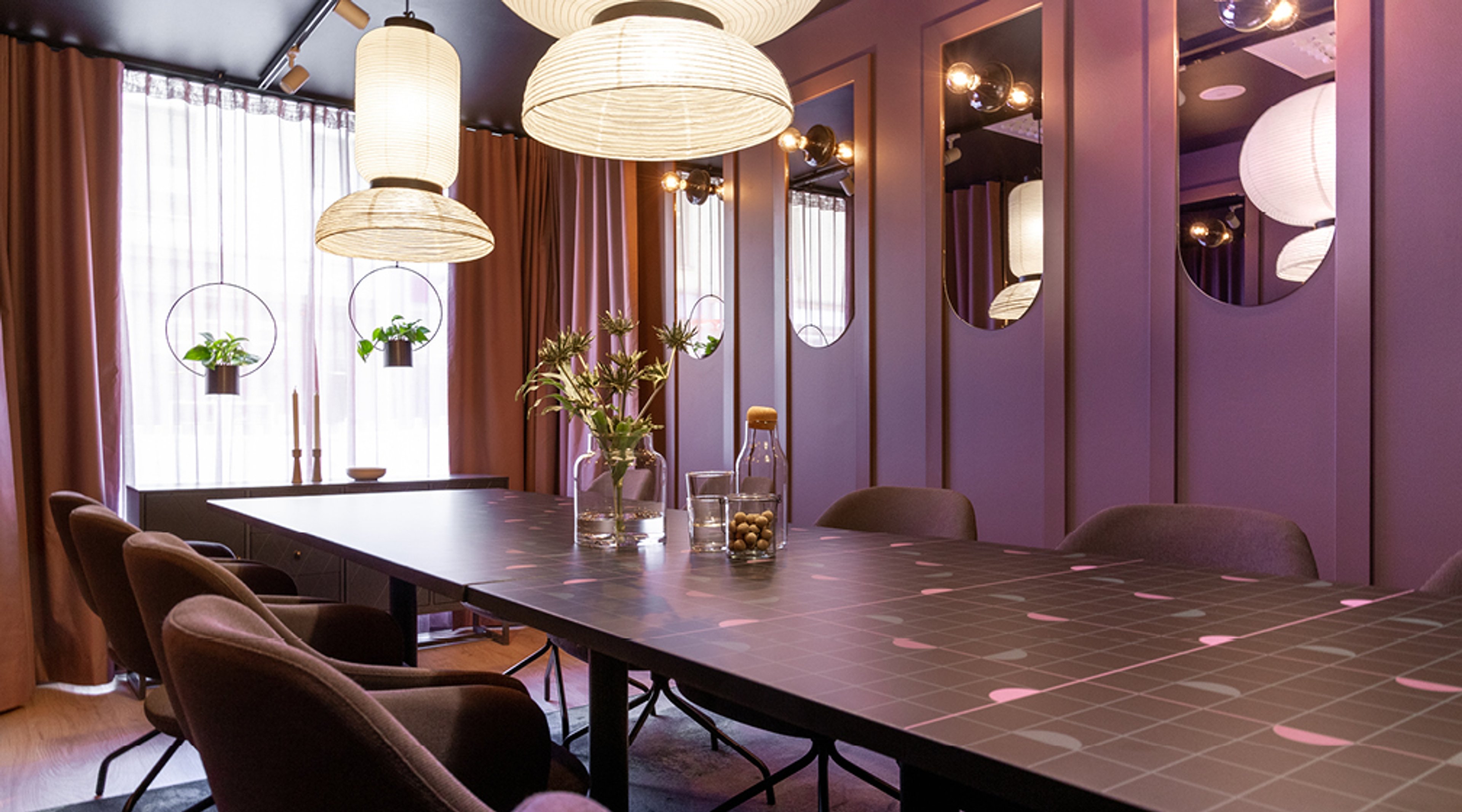 Moderni neuvotteluhuone violettiseinillä, tumma laattapöytä, mukavat tuolit, riippuvalaisimet ja pyöreät peilit.