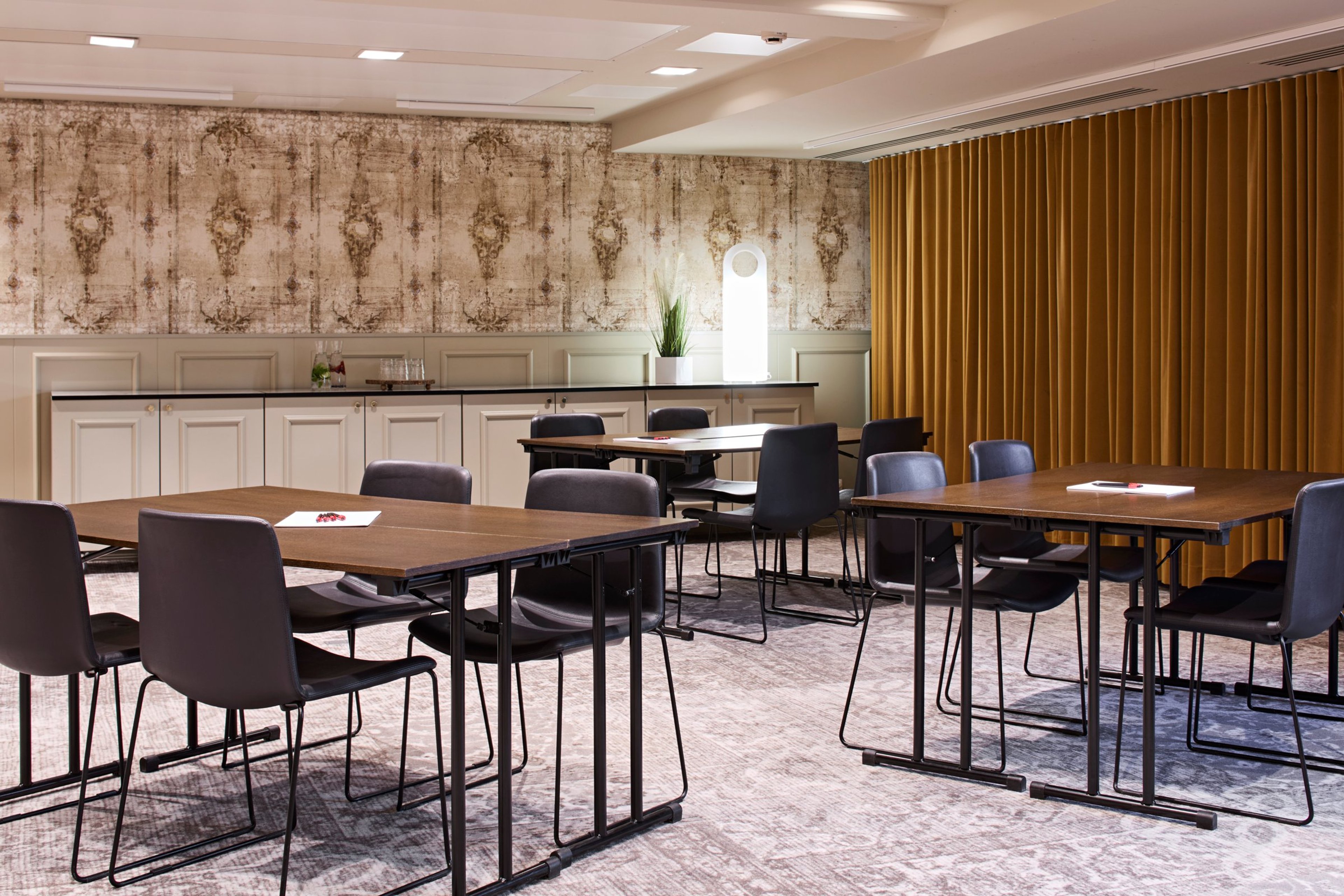 Kokoushuone, jossa on puiset pöydät ja tummat tuolit. Takaosassa on tarjoilupöytä. Seinällä koristeellinen tapetti ja oranssi verho.