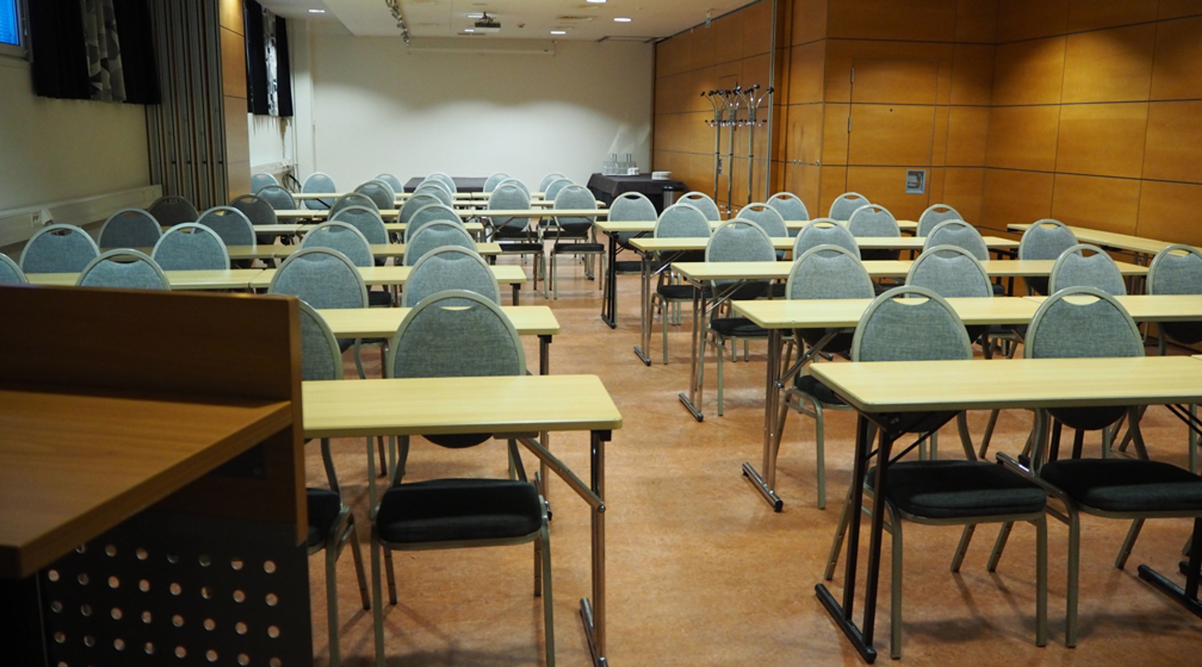 Koulutustila, jossa on rivittäin pöytiä ja sinisiä tuoleja. Tilan seinät ovat puupaneloituja ja lattialla on korkkilaatta.