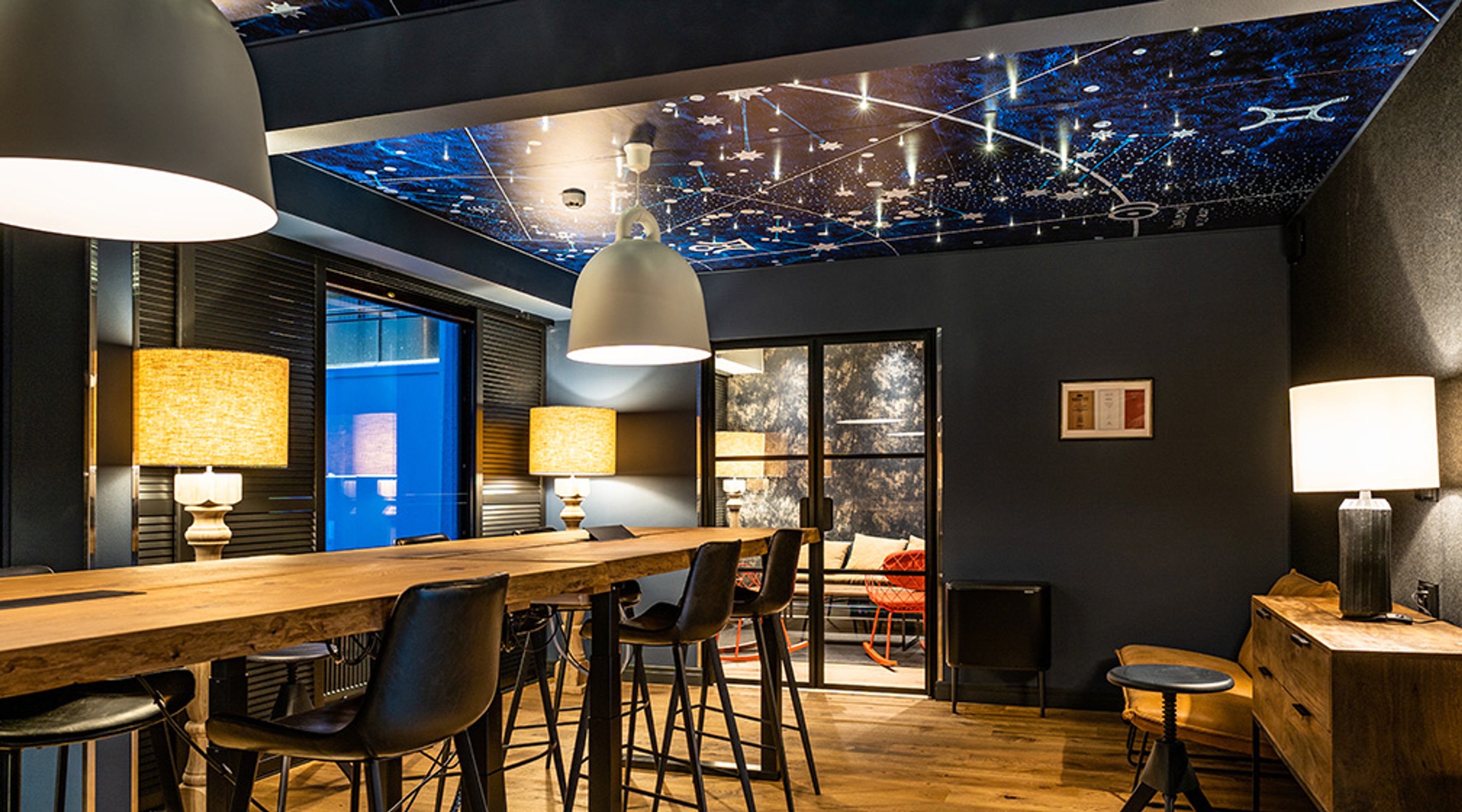 Moderni kokoustila, jossa tähtikattomainen valaistu sisäkatto, puinen baaripöytä korkeilla tuoleilla ja lämmin valaistus.