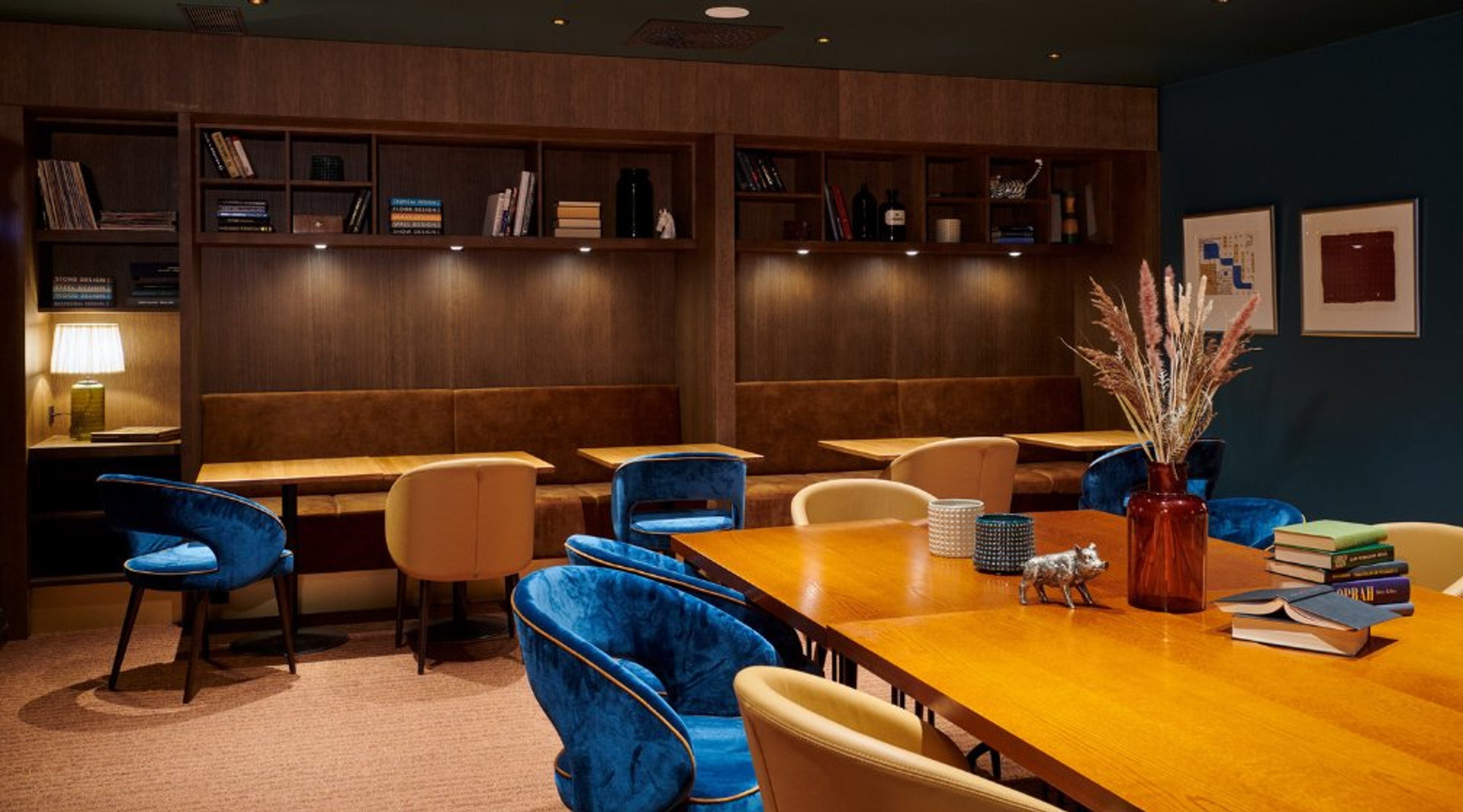 Stylishly furnished meeting room with wooden table, blue and cream chairs, bookshelves, and low-pile carpet flooring.