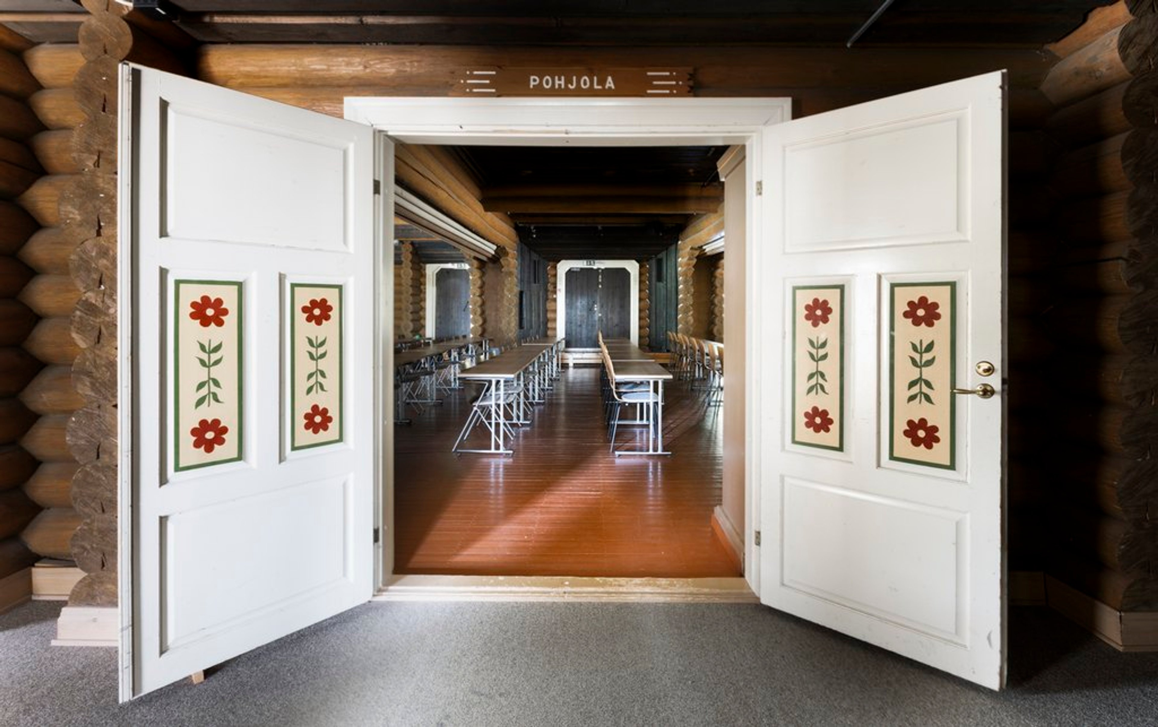Two wide doors opened to a log room with glossy floors, rows of folding tables and chairs.