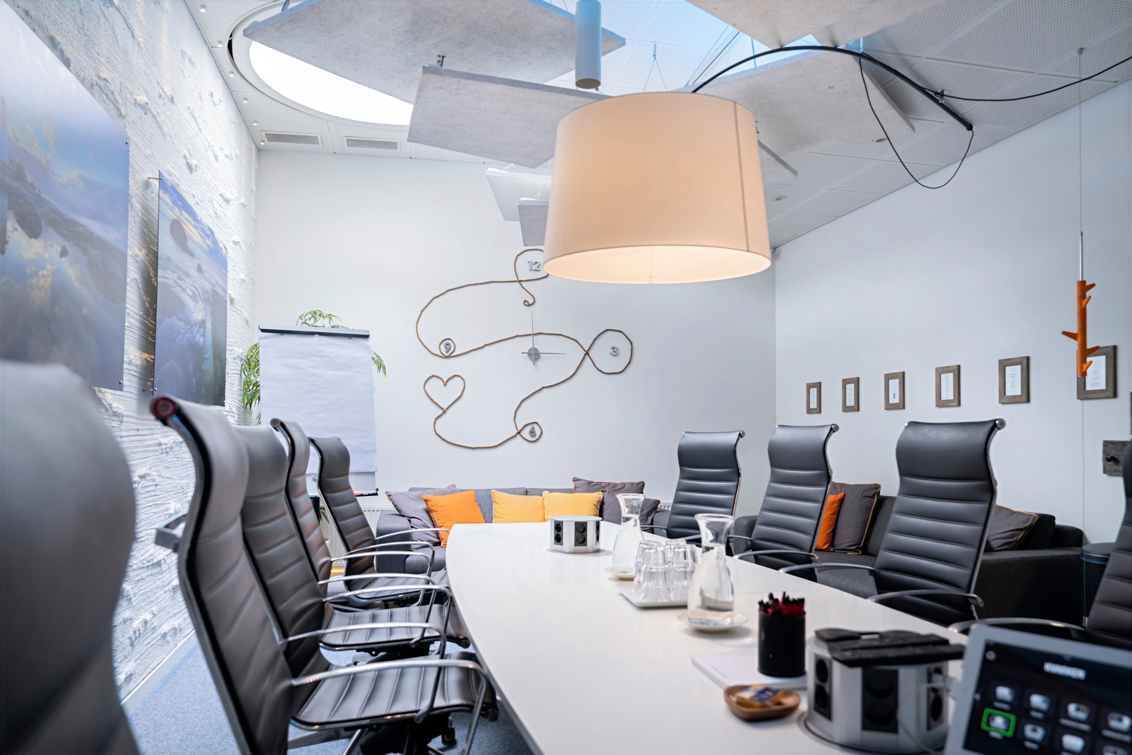 Modernisti sisustettu neuvotteluhuone, jossa valkoinen pöytä, mustia tuoleja, värikkäitä tyynyjä sohvalla ja suuri valaisin katossa.