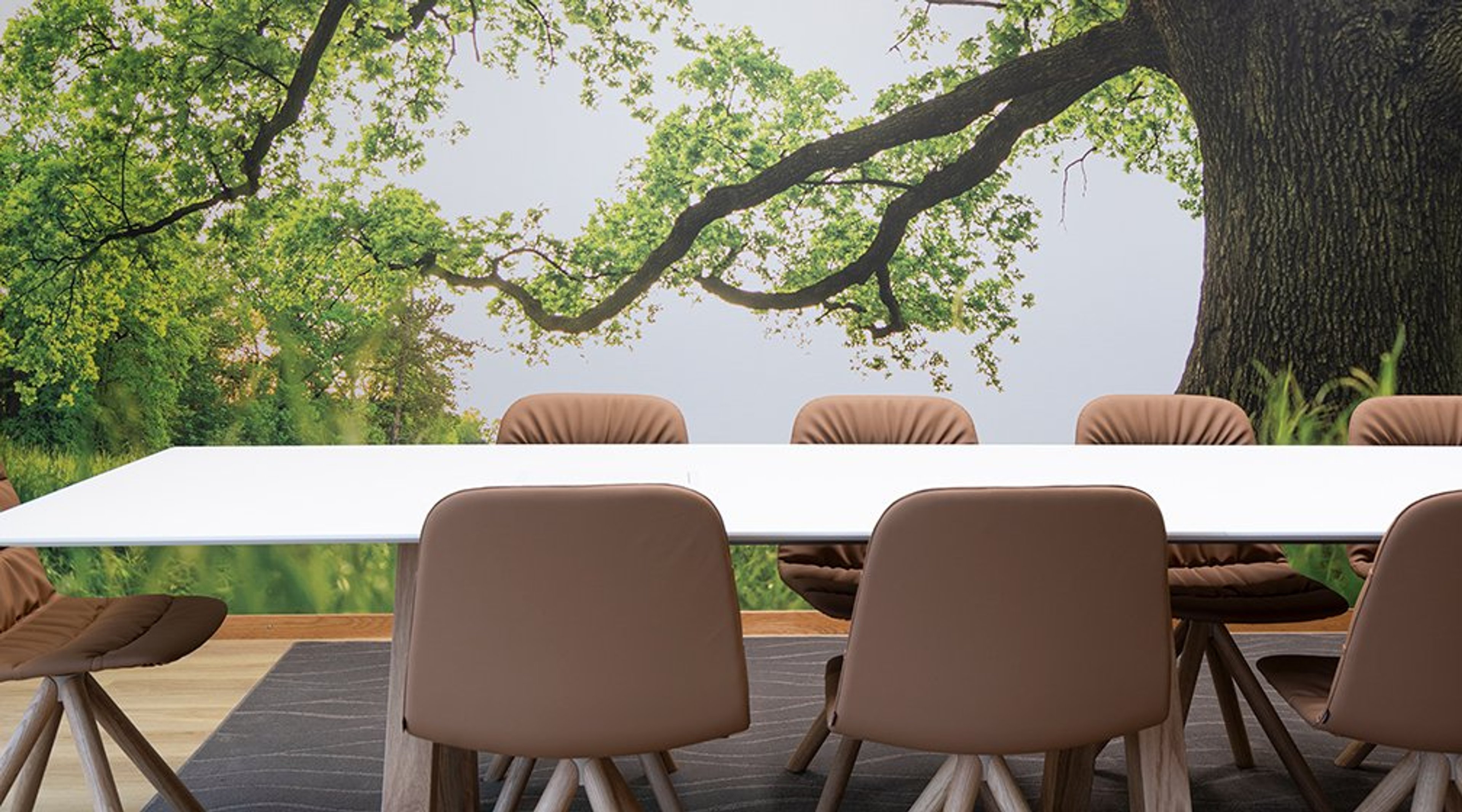 Valkoinen neuvottelupöytä ja ruskeat tuolit ulkoterassilla, taustalla vehreä puu ja luontomaisema.