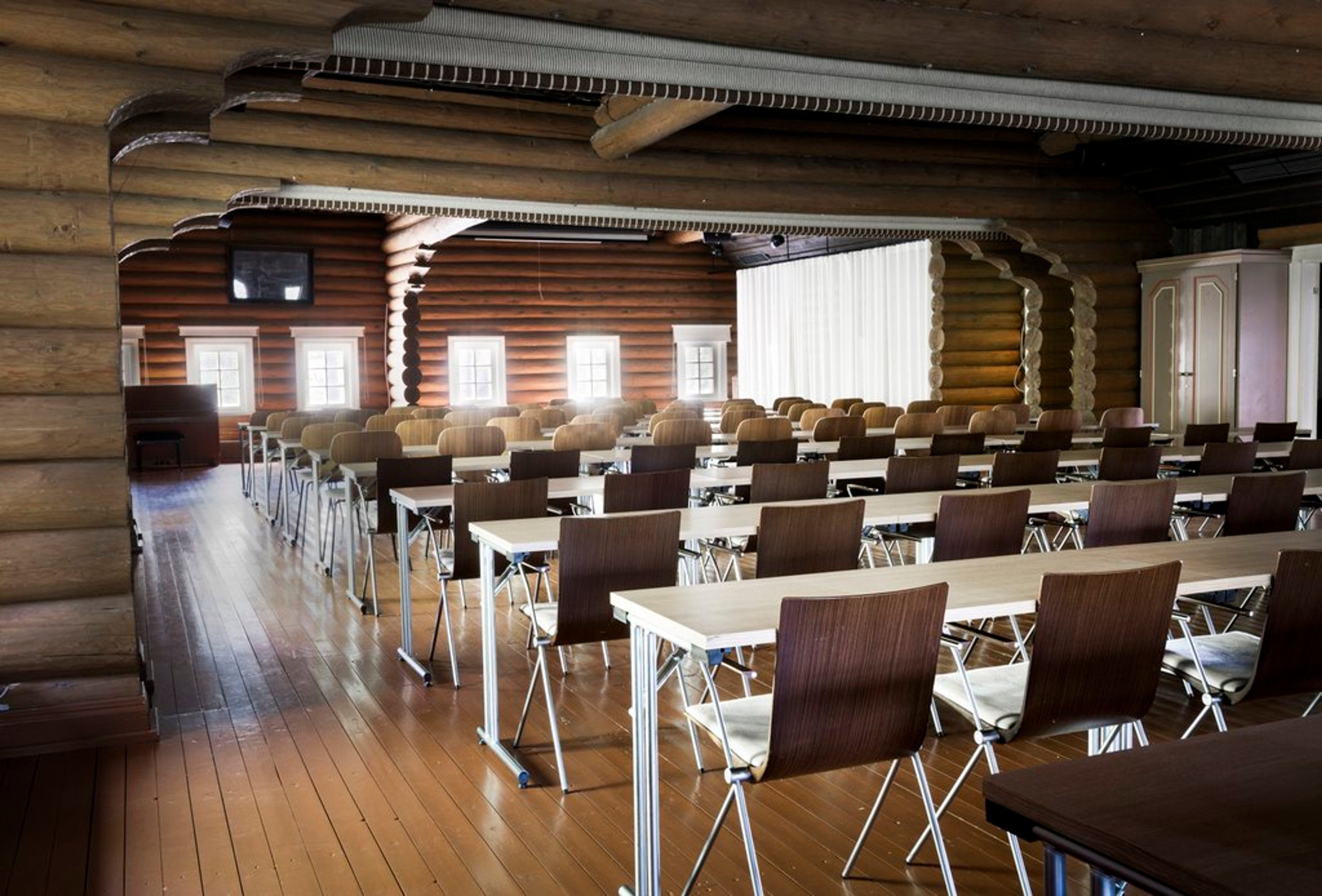 Conference room with log walls, rows of white tables and brown chairs on a polished wooden floor.