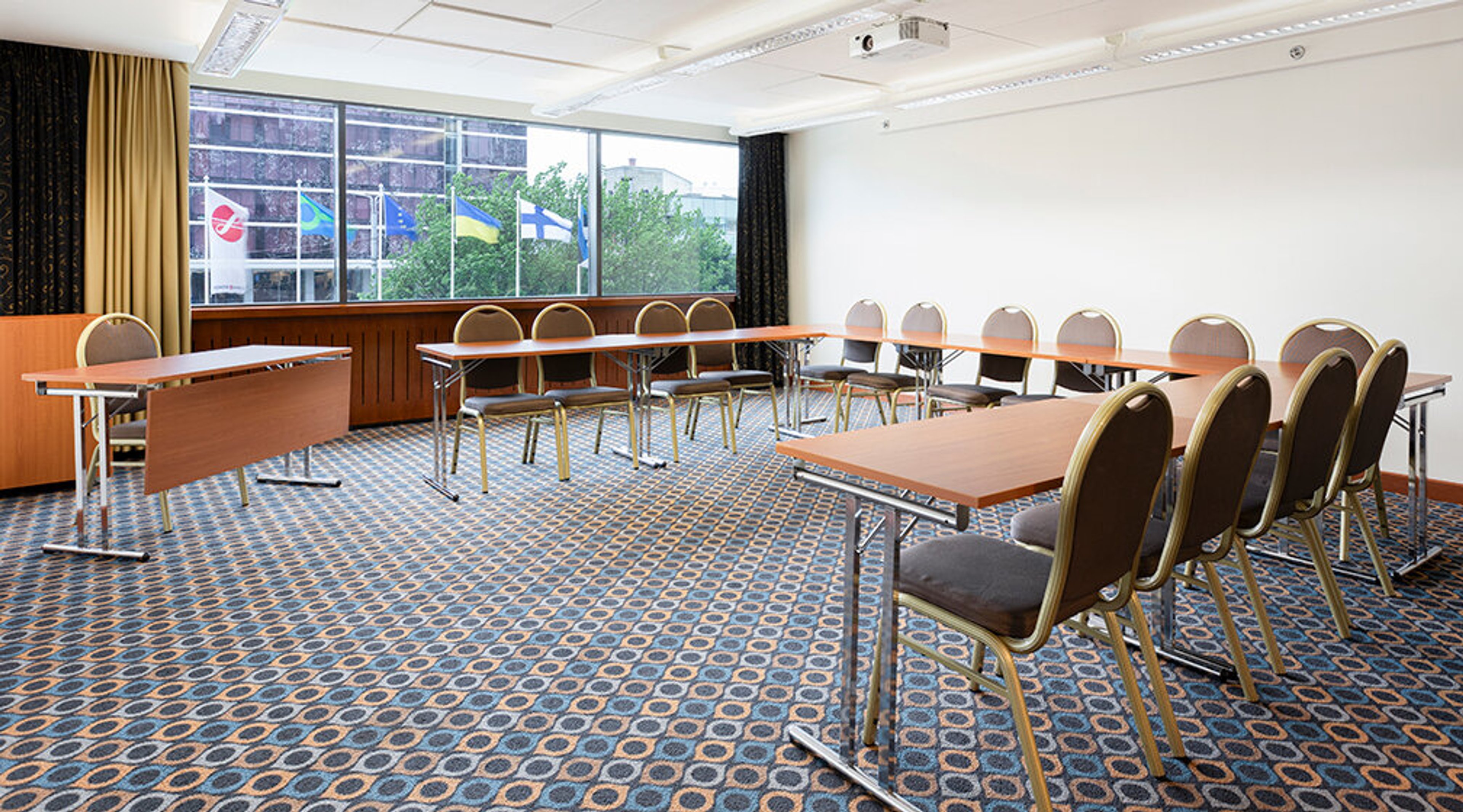 Conference room with tables and chairs arranged in rows. The space is bright, and the floor has patterned carpeting.