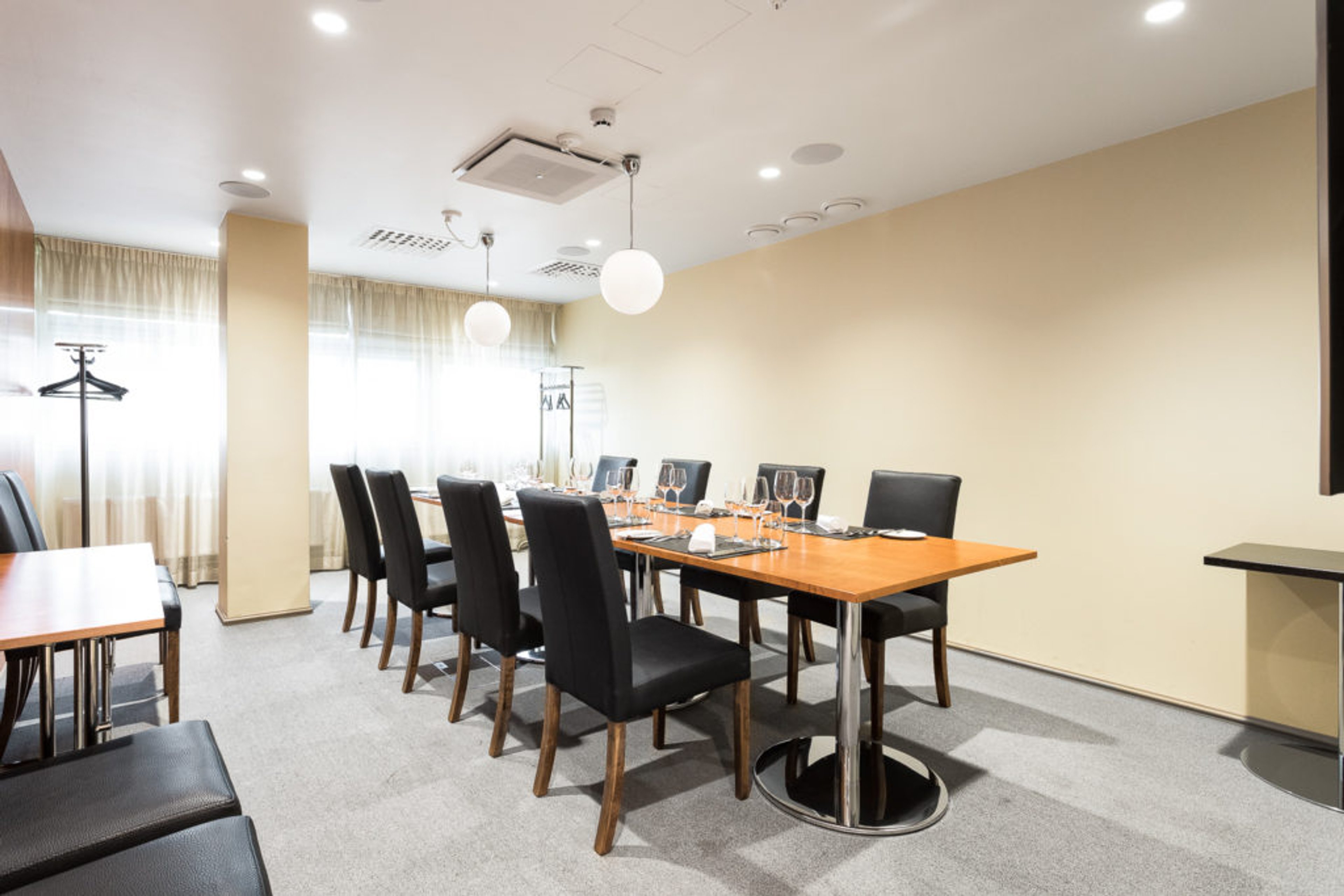 Ljust mötesrum med långt träbord, svarta stolar, vinglas och servering. Rummet har ljusa väggar och hängande lampor.
